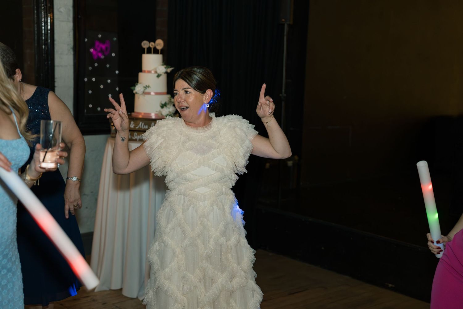 Wedding guests dancing under colorful lights during an evening reception celebration.
