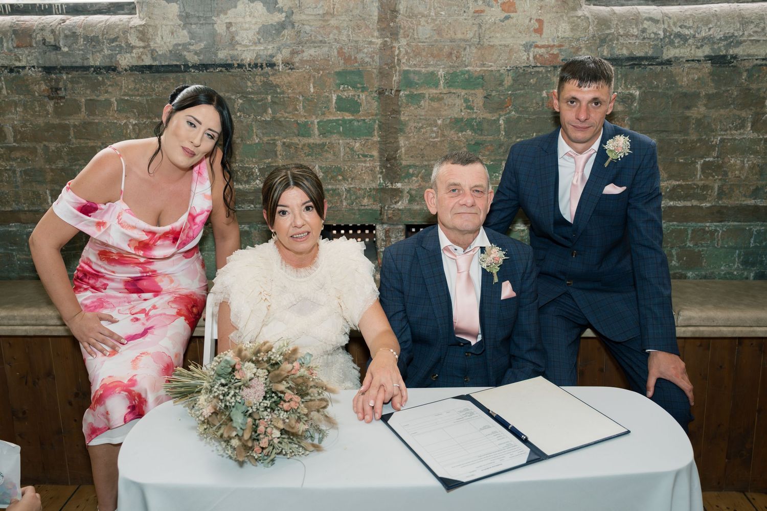 Wedding couple signing documents at a white table in a historic brick venue.