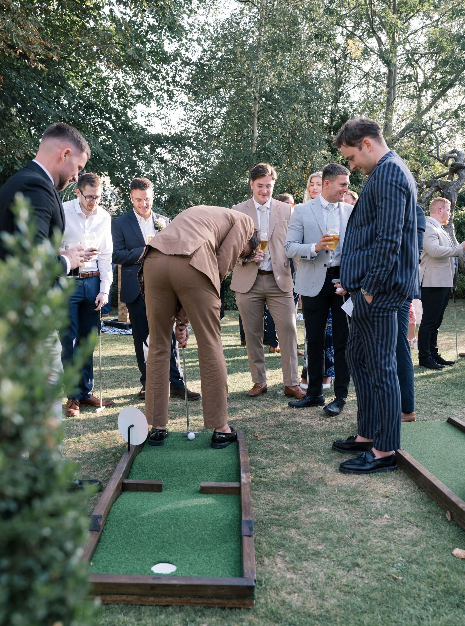 Wedding guests playing miniature golf on portable putting greens set up on grass.