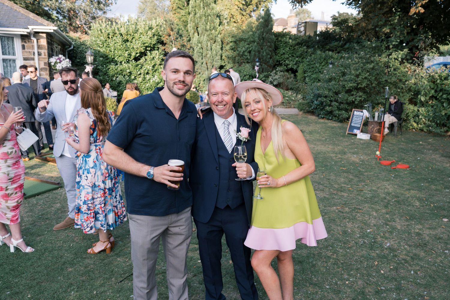 Wedding guests gather for casual photos in garden setting with drinks.