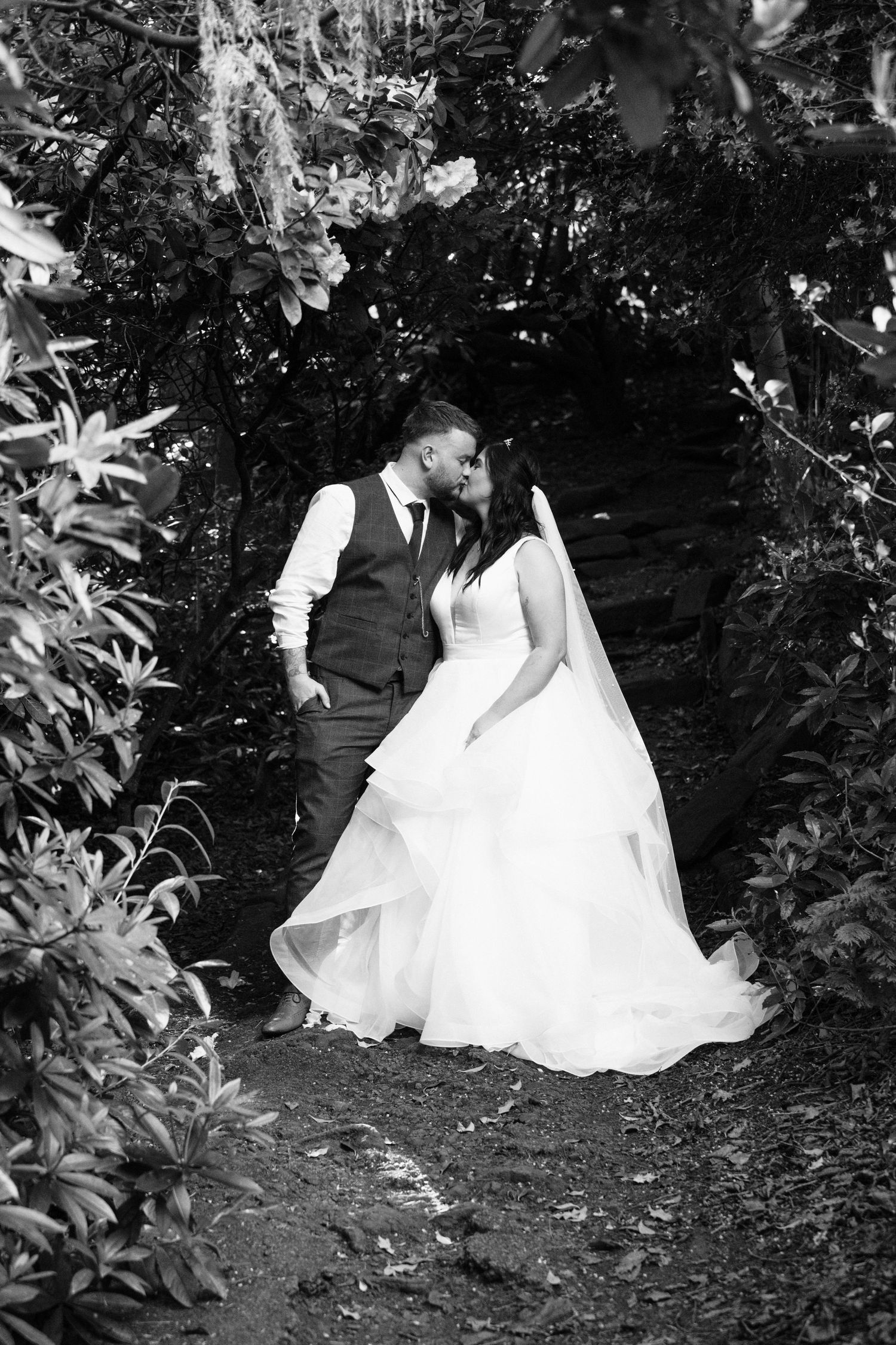 Artistic black and white garden portrait of wedding couple on a nature path.