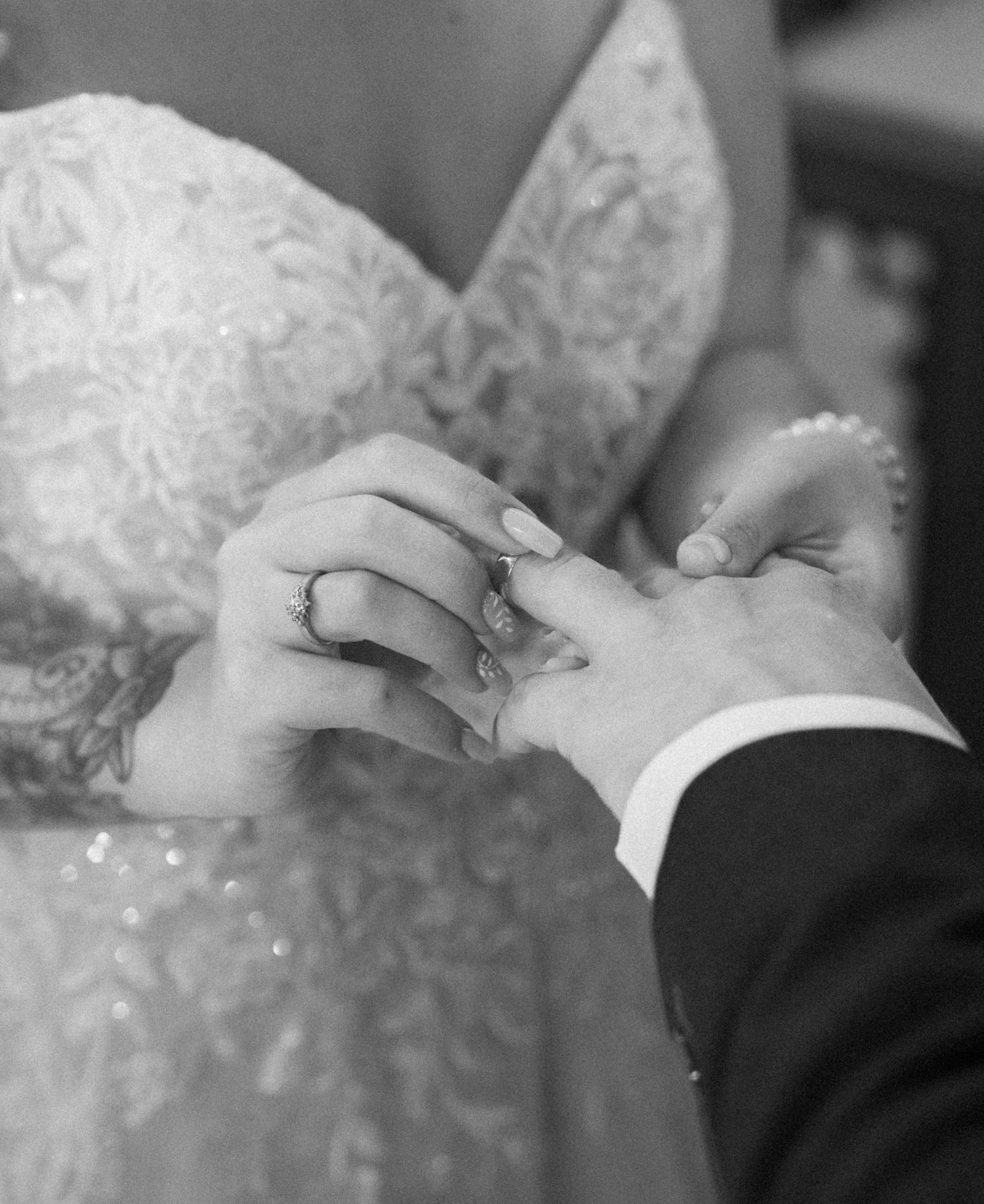 A close-up black and white photograph of hands exchanging wedding rings during a ceremony.