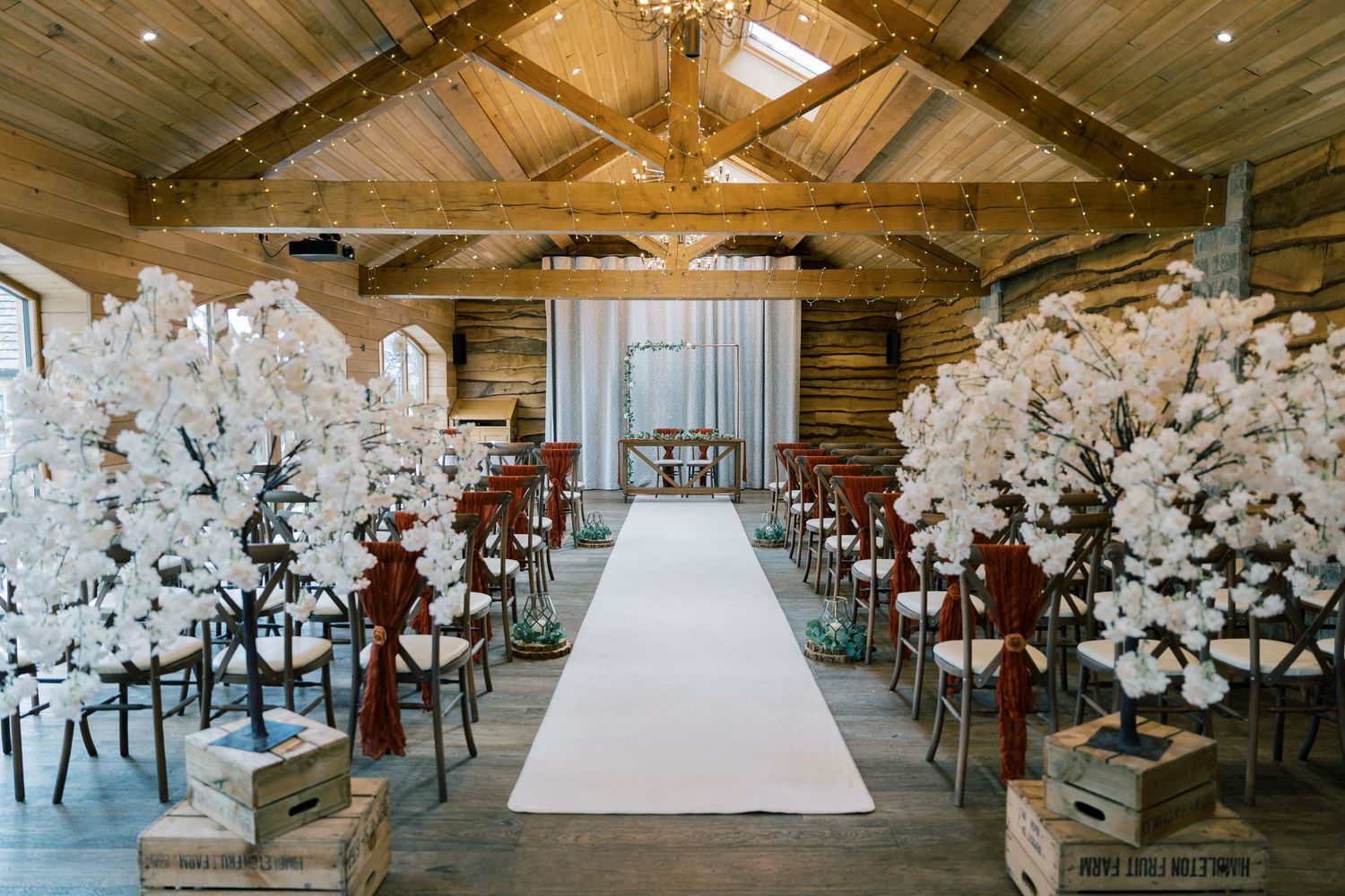 Wedding ceremony setup in rustic wooden barn with white floral decorations lining aisle.