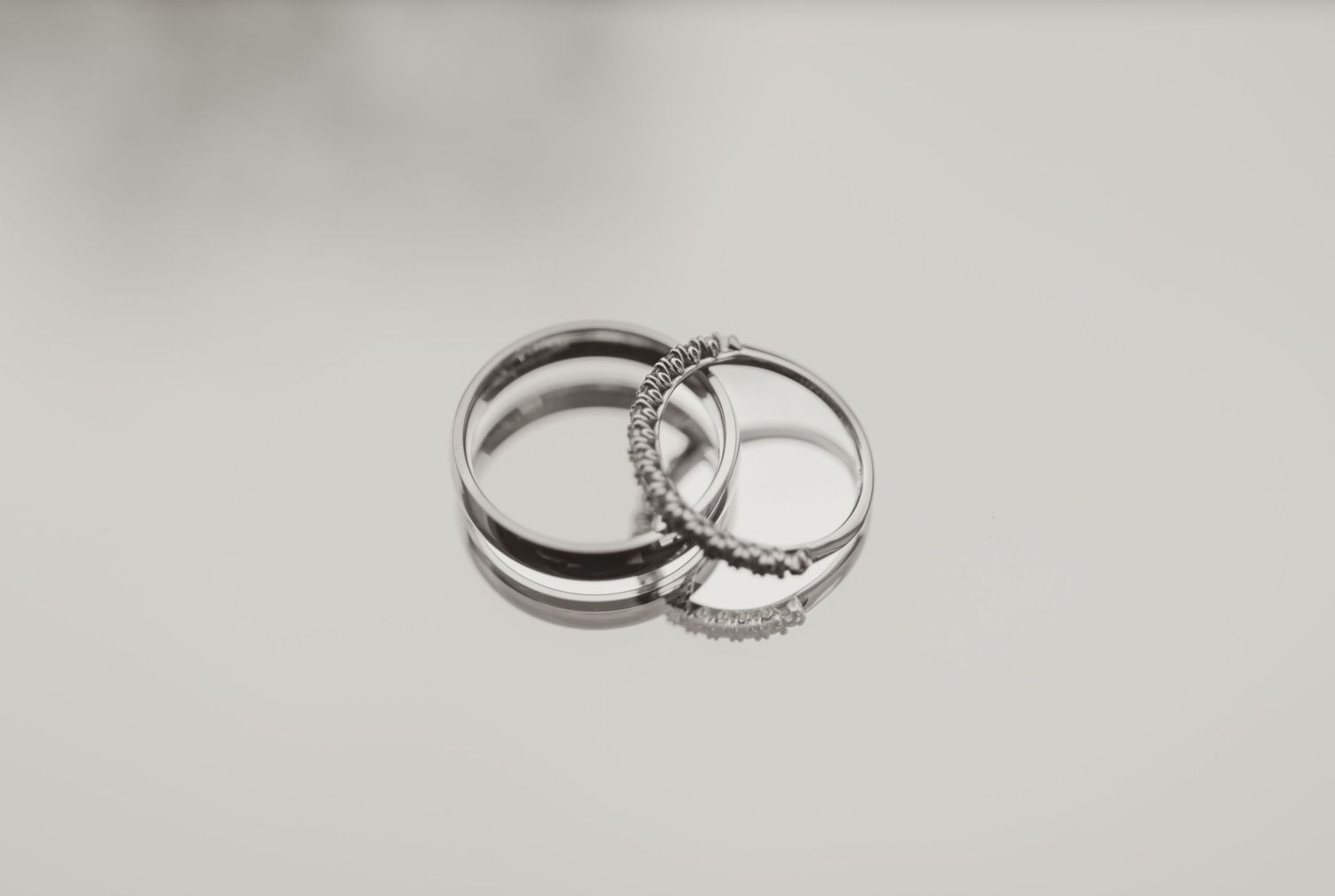 Three silver rings with diamond accents stacked together on a white reflective surface.
