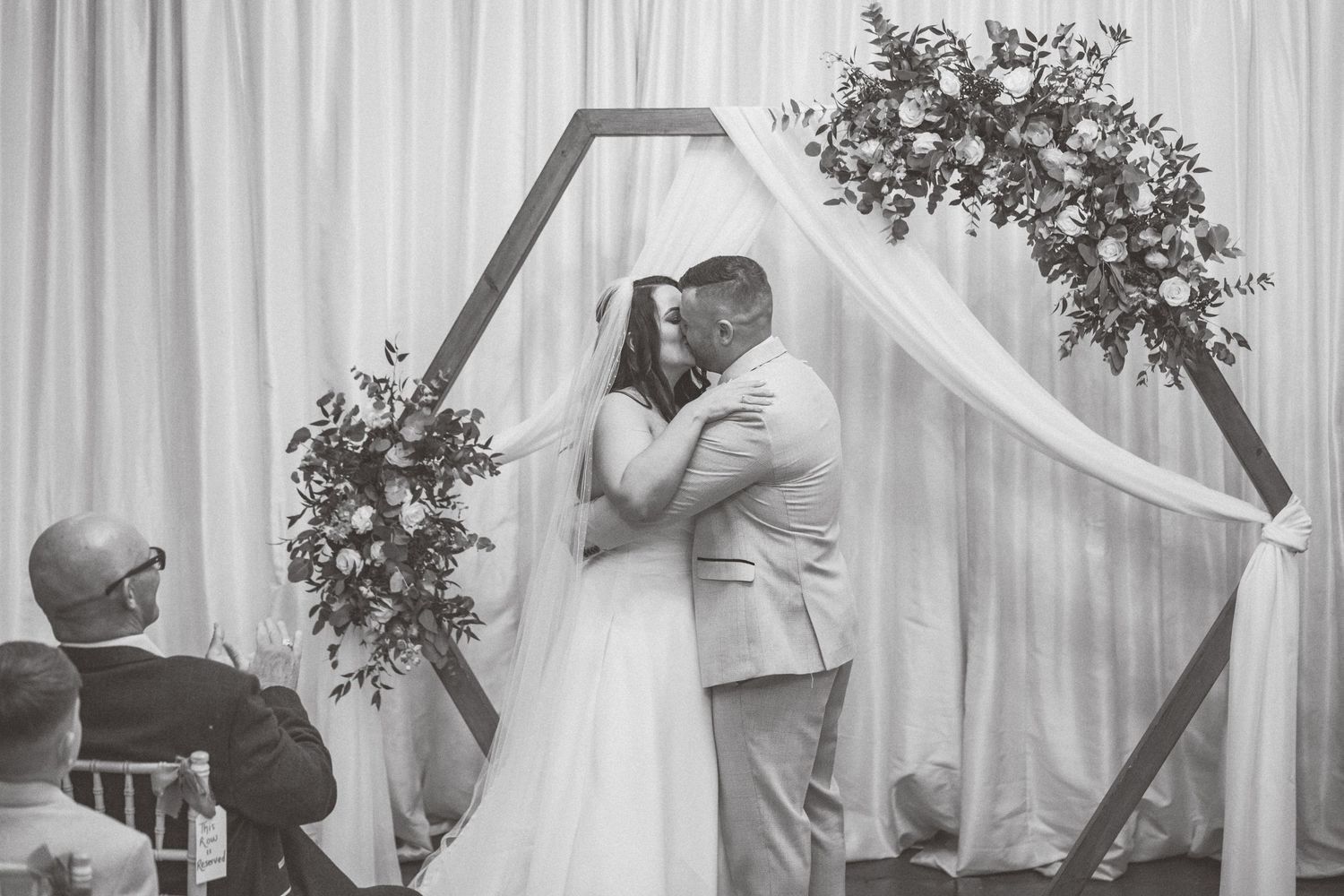 Black and white wedding ceremony photos showing couple at altar with decorative arch and white draping.
