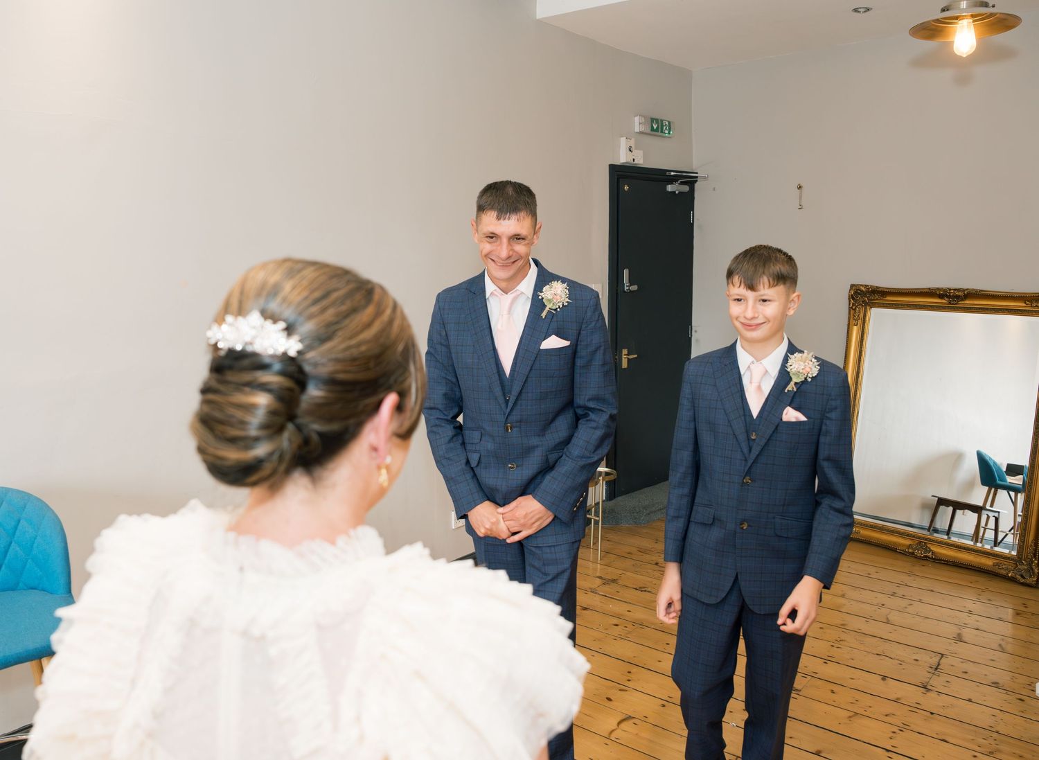 Wedding party poses in a bright indoor space with wooden floors and white walls.