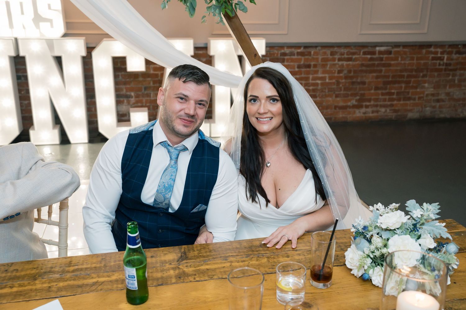 Newlyweds share a moment at their reception table with exposed brick walls and elegant decor.