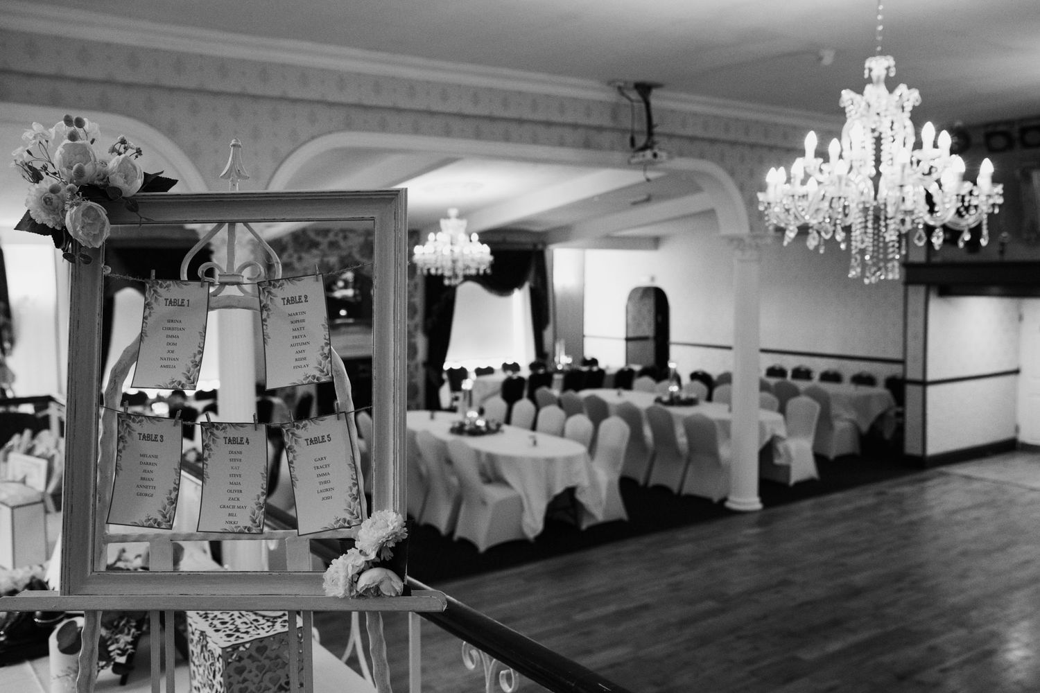 An elegant reception hall with crystal chandeliers and white-covered chairs arranged for a wedding celebration.