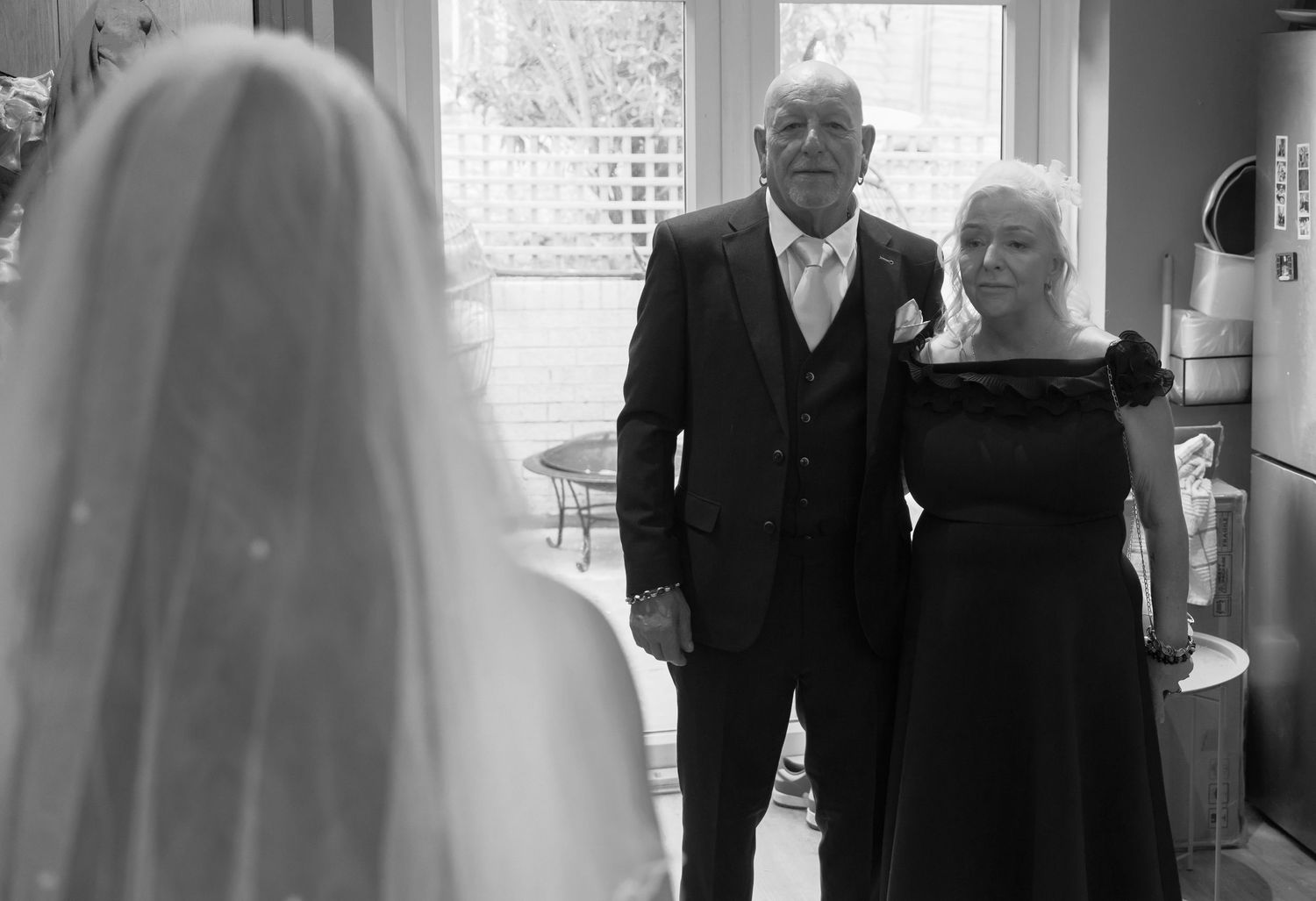 A tender moment as two people watch someone in a bridal veil during a wedding ceremony in a beautifully lit room.