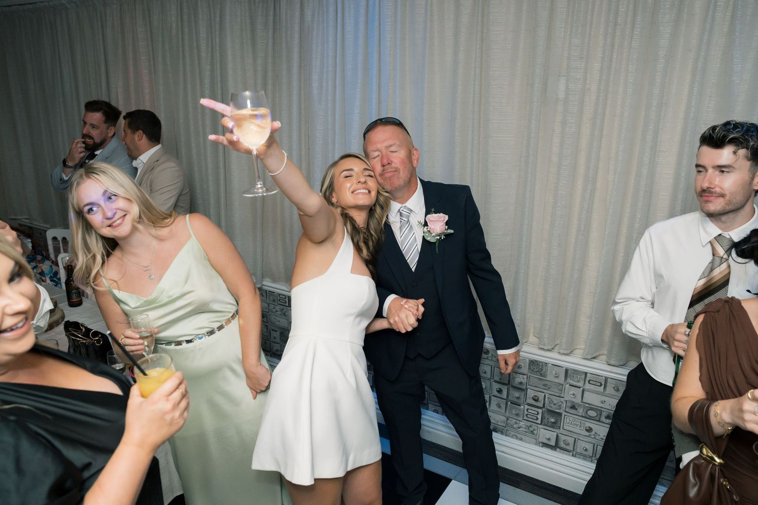 Wedding party dancing and celebrating in formal attire at indoor reception.