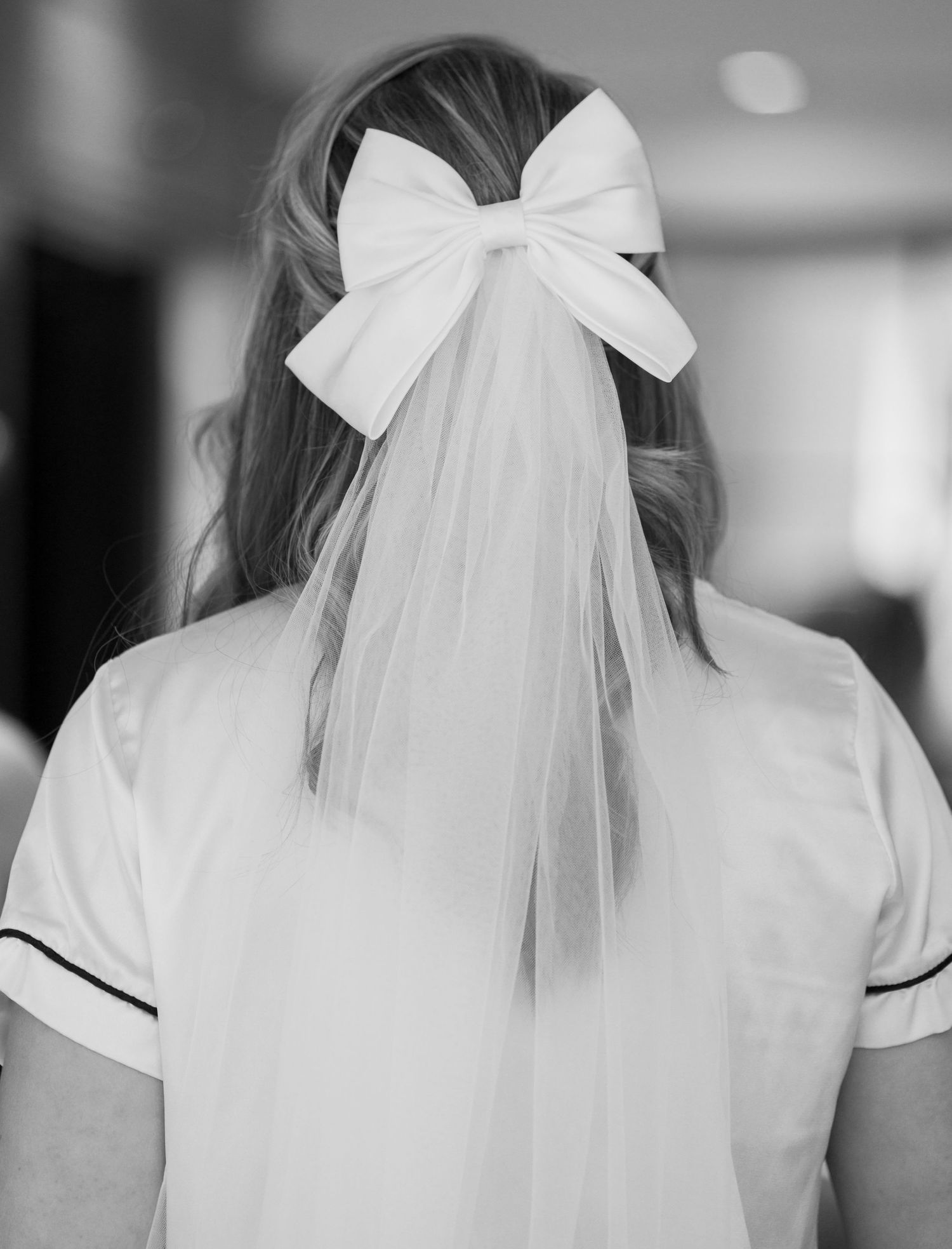 A black and white photo showing the back of a bridal veil with a large white bow hair accessory.