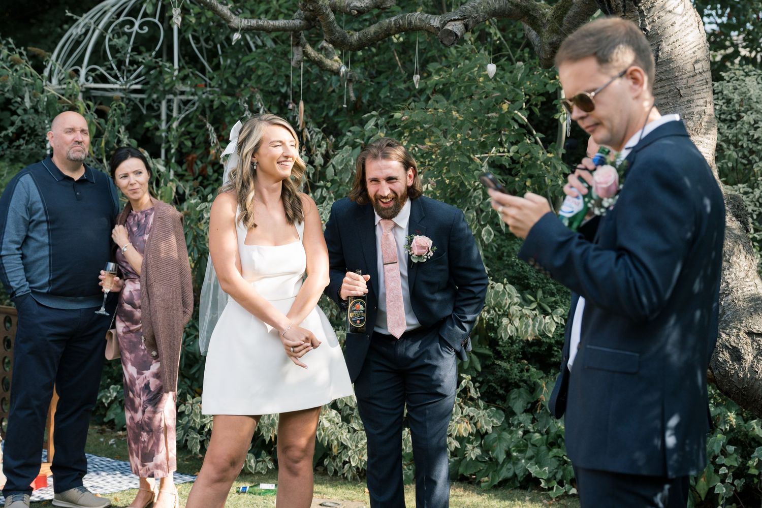 Casual outdoor wedding ceremony with guests gathered in a garden setting.