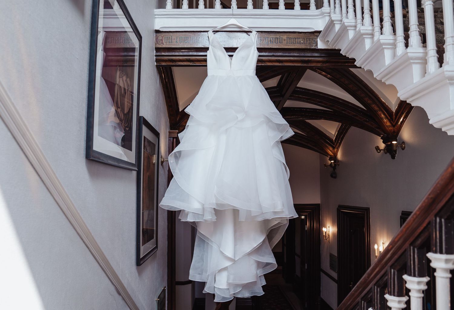 White wedding dress hanging on display in a stairwell with wooden bannisters.