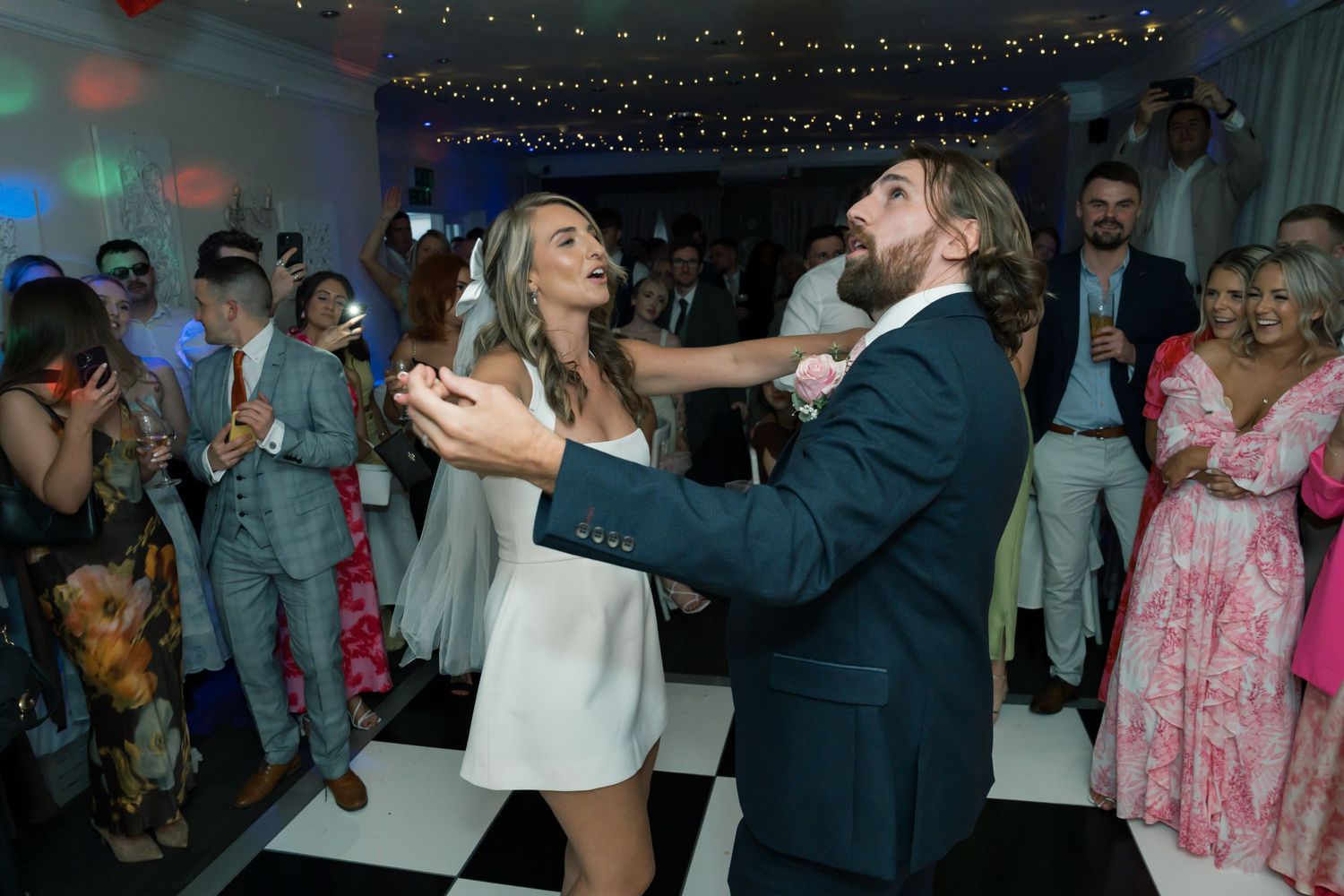 Wedding reception dance party with string lights overhead and guests dancing in celebration.