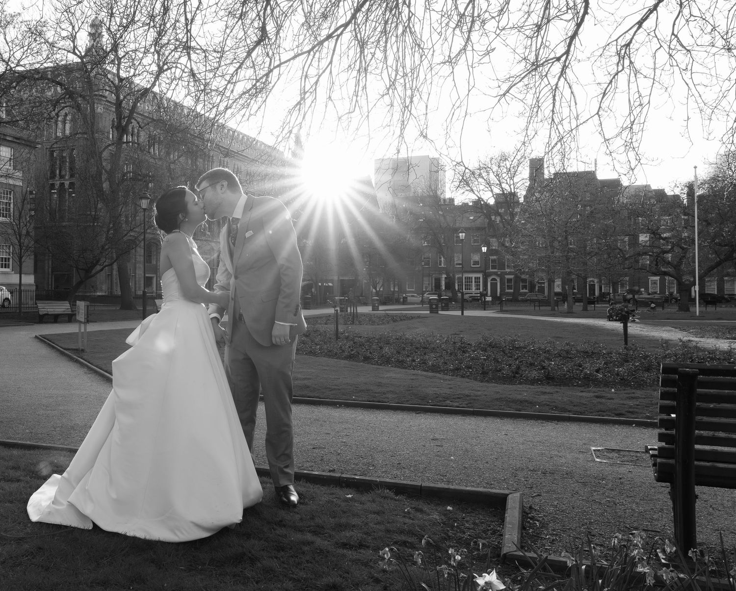A romantic black and white wedding photo series showing a couple in a park with sunlight streaming through trees.