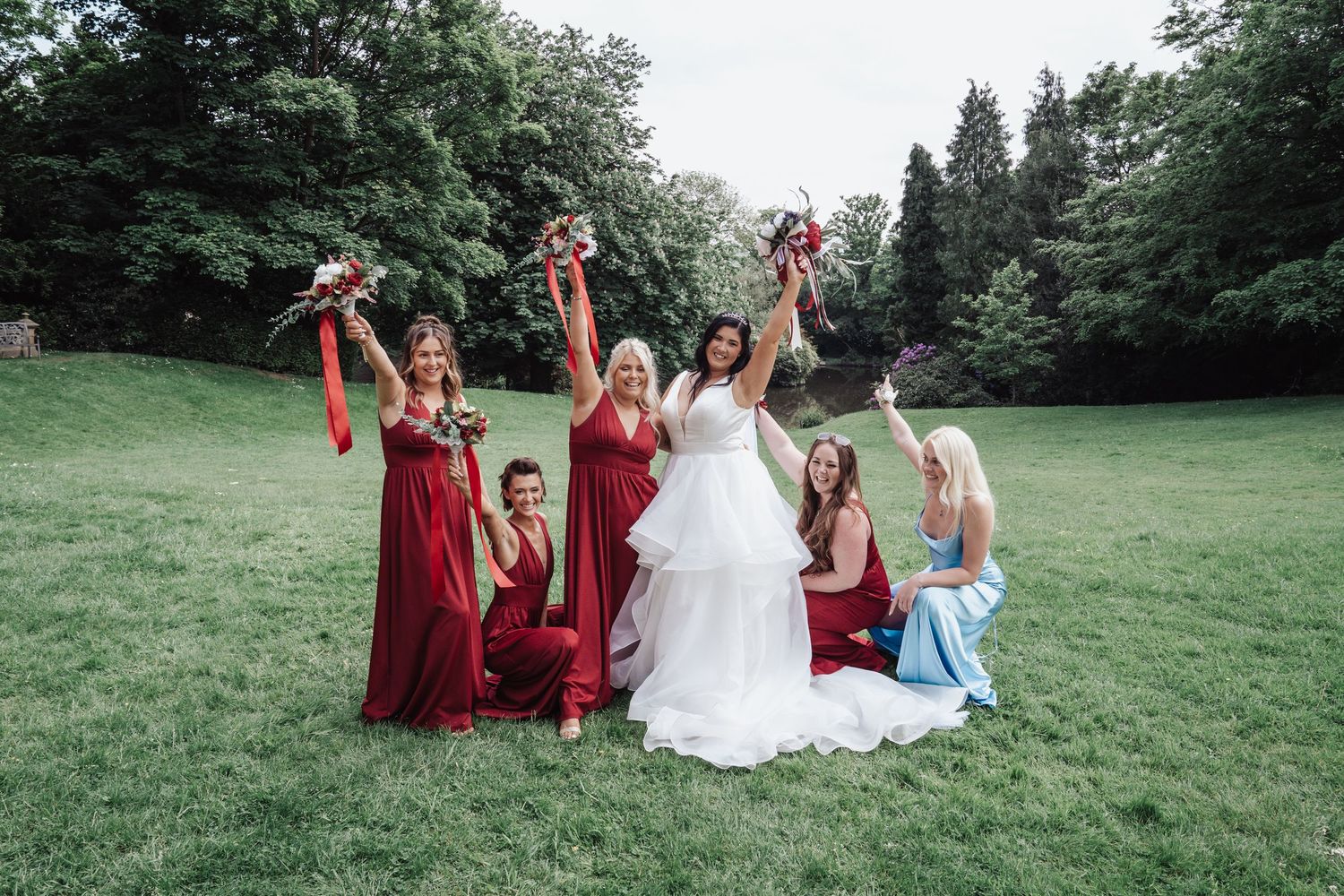 Wedding party celebrating outdoors with bridesmaids in burgundy dresses on a grassy lawn.