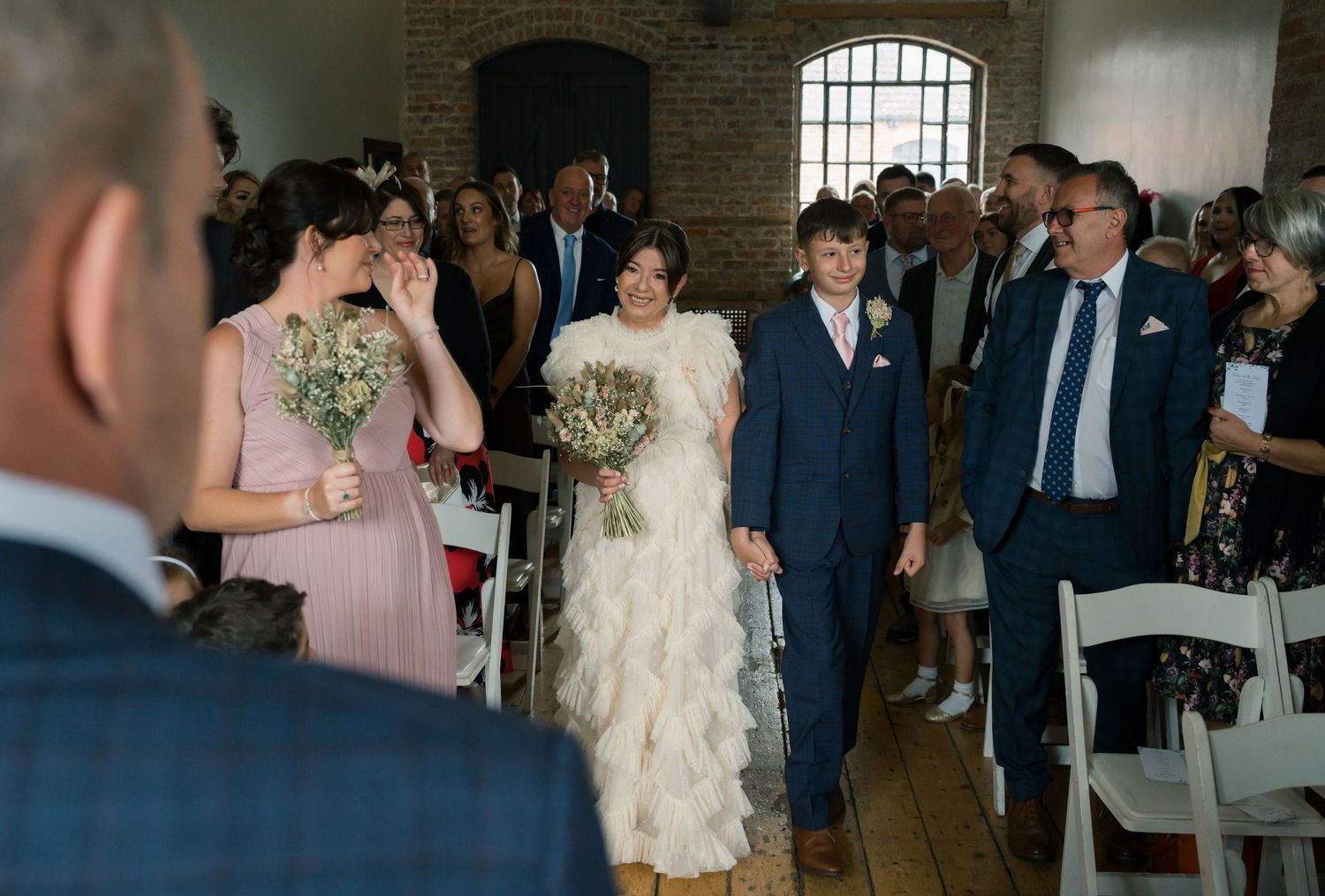 Wedding ceremony guests gather in rustic brick venue with natural lighting.