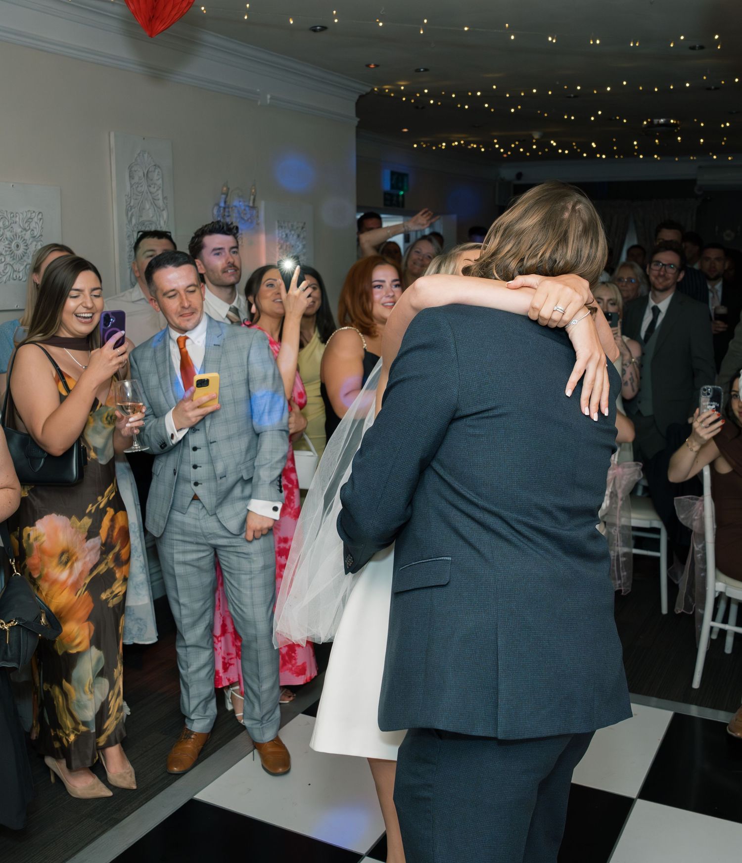 Wedding guests dancing and celebrating at an indoor reception with string lights.