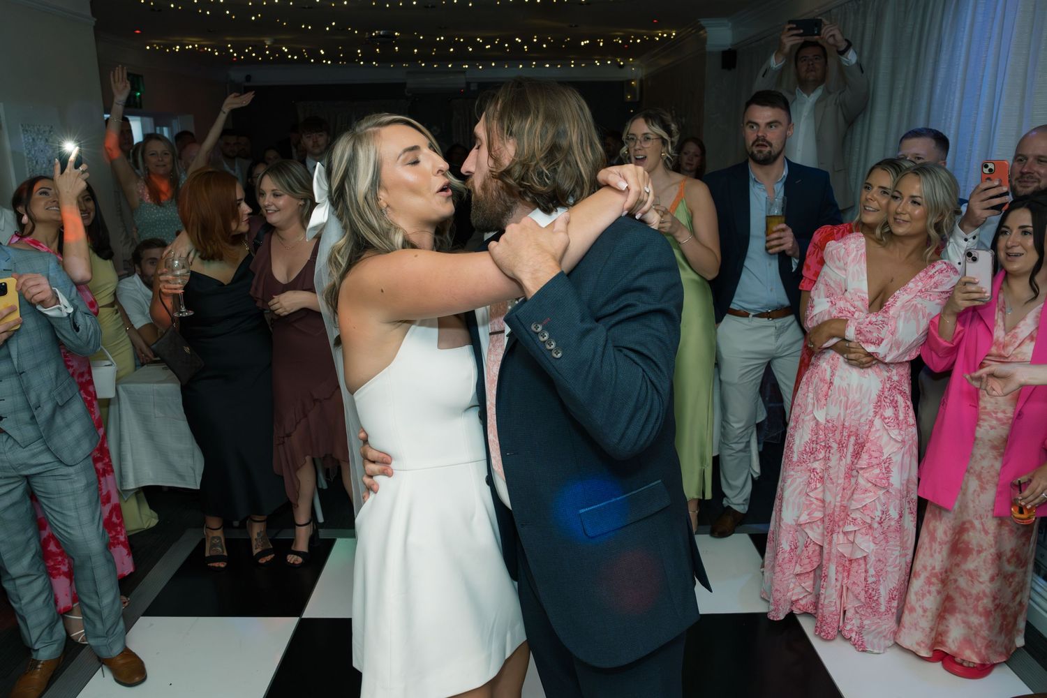 Wedding reception dance floor filled with guests celebrating under string lights.
