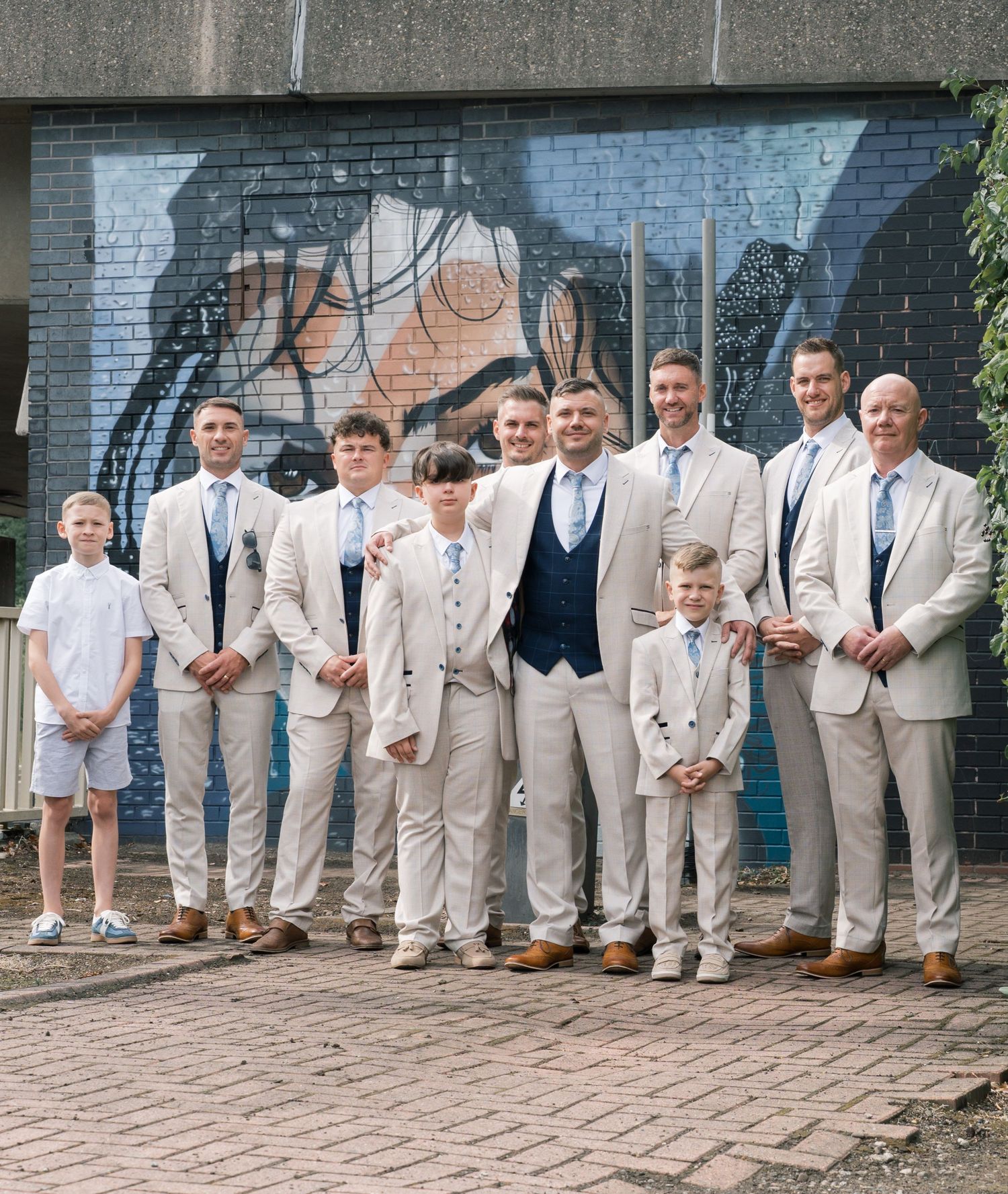 Groomsmen in light beige suits strike playful poses against a brick wall in a series of candid wedding photos.