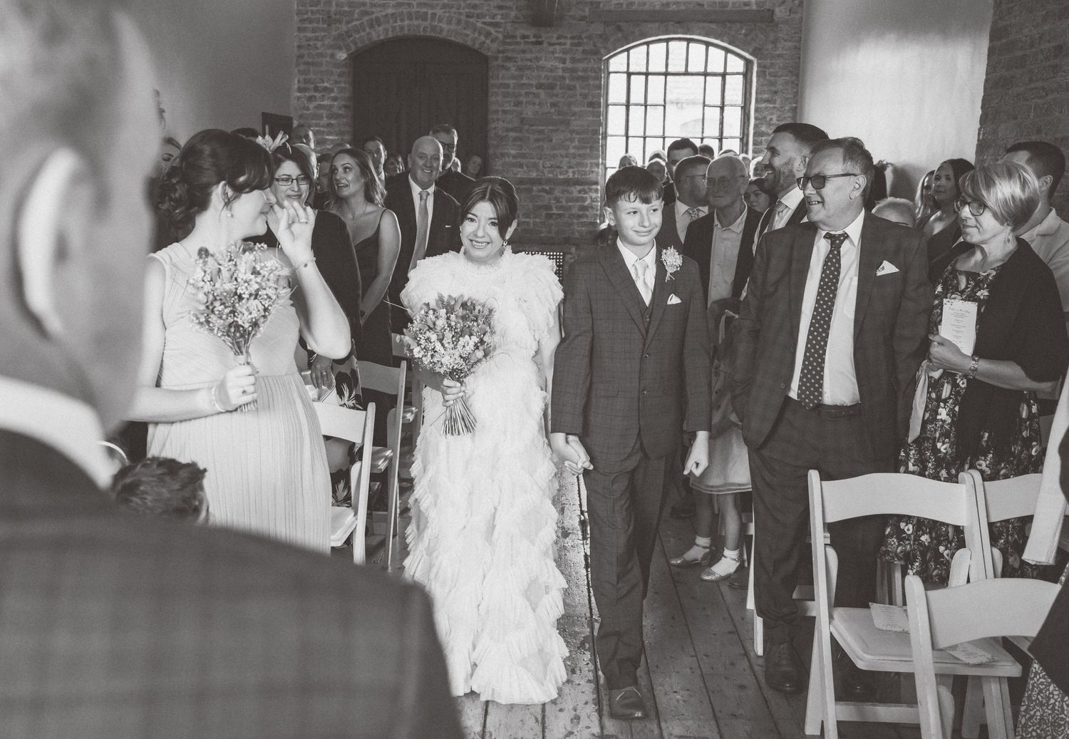 Black and white photo of wedding ceremony in industrial brick venue with guests.
