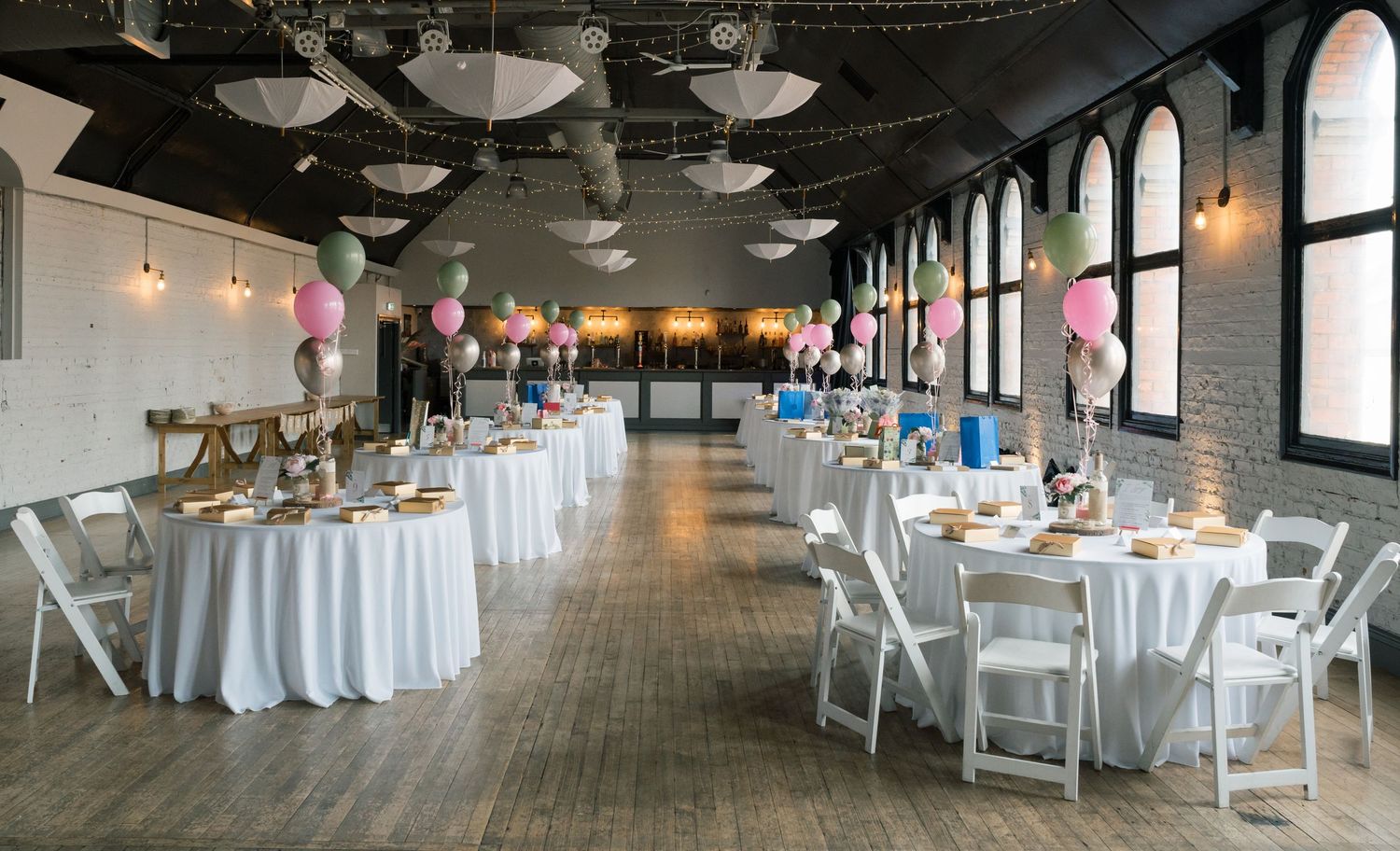 Elegant wedding reception venue with rustic wood floors, white tablecloths, and hanging pendant lights creating a romantic ambiance.