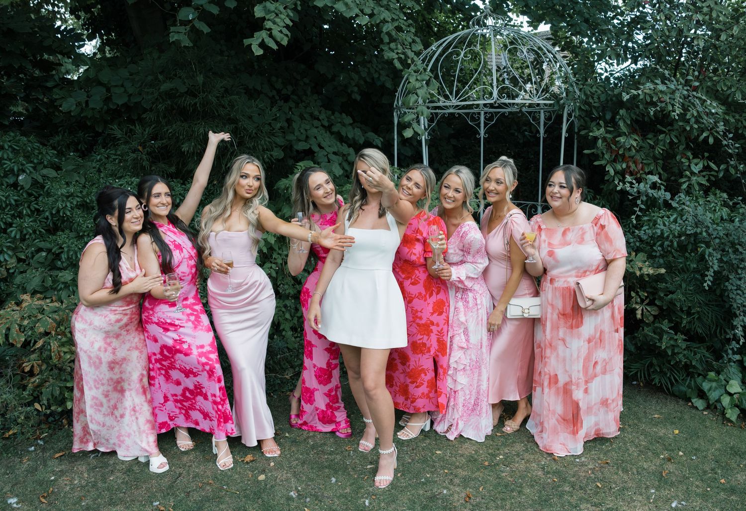 A group wearing pink and coral dresses poses together outdoors during a special celebration event.