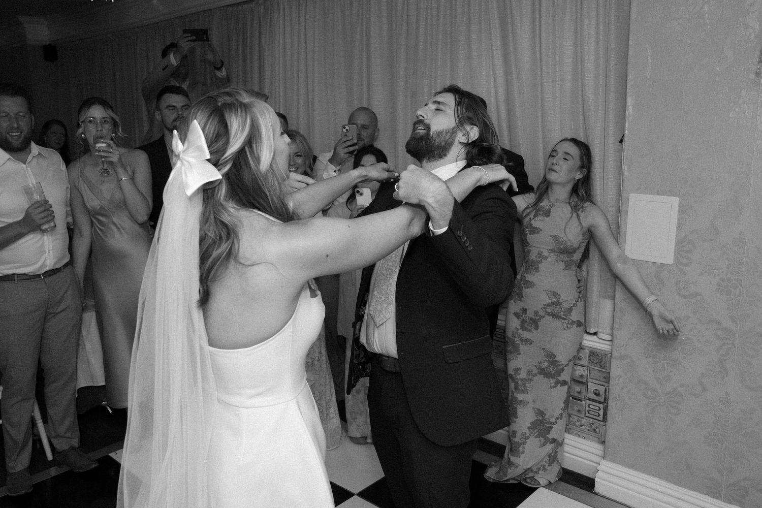 A black and white photo of newlyweds dancing and celebrating at their wedding reception.