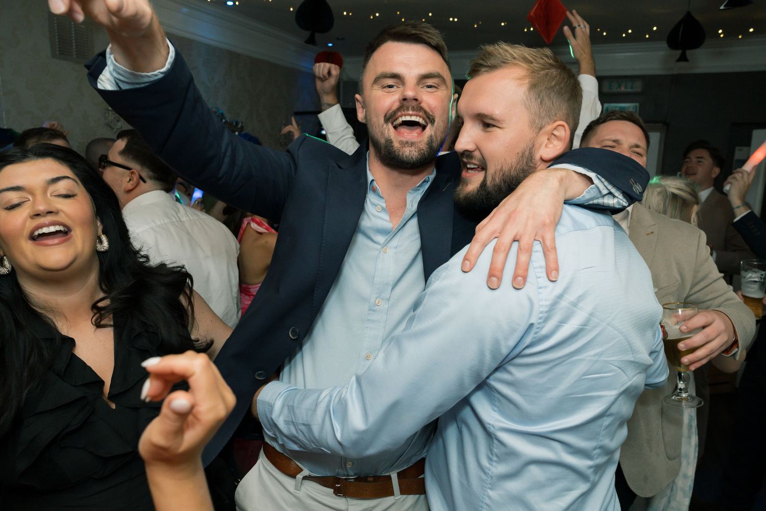 Energetic celebration scene with party guests hugging and cheering in dimly lit venue.