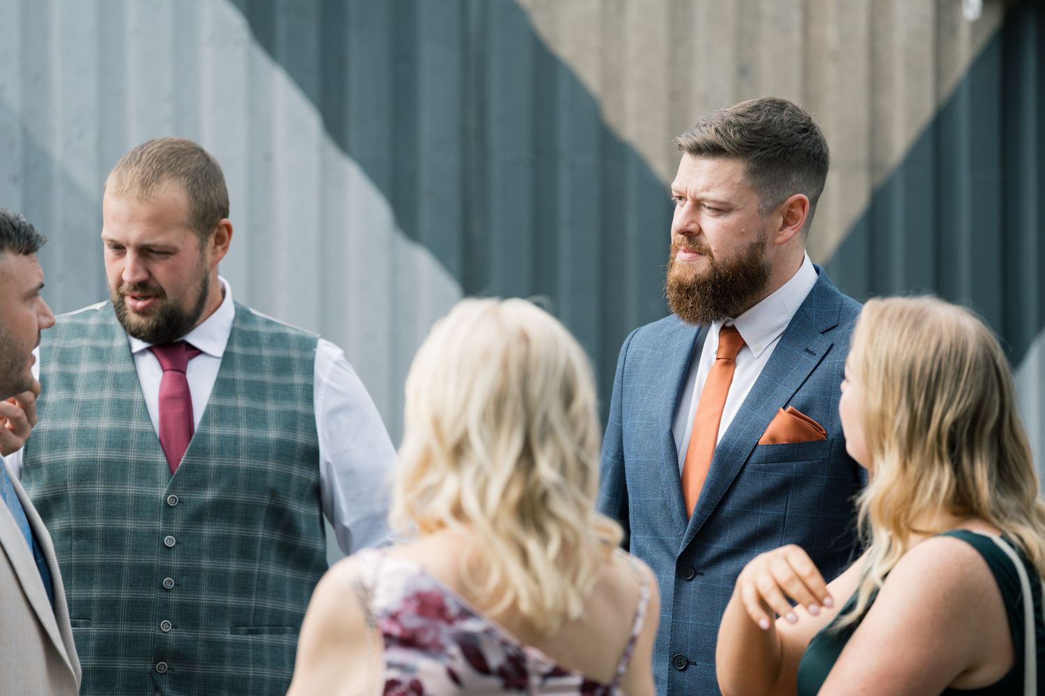 Wedding guests mingle and socialize during an outdoor cocktail reception with exposed brick wall backdrop.