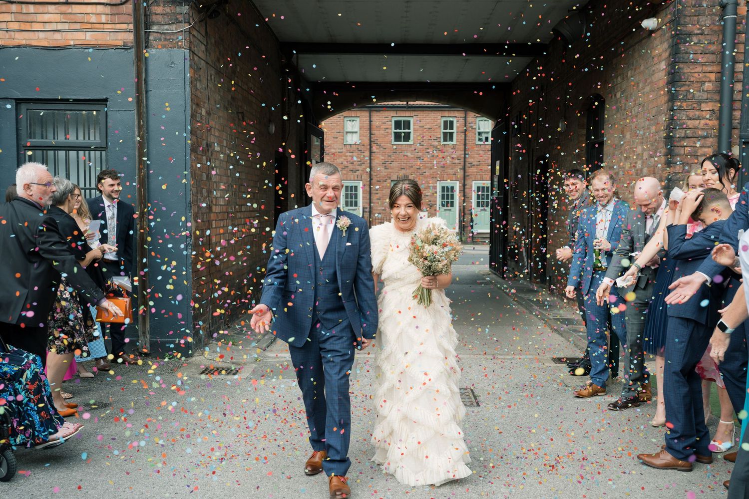 Wedding exit with confetti throw outside historic brick building.