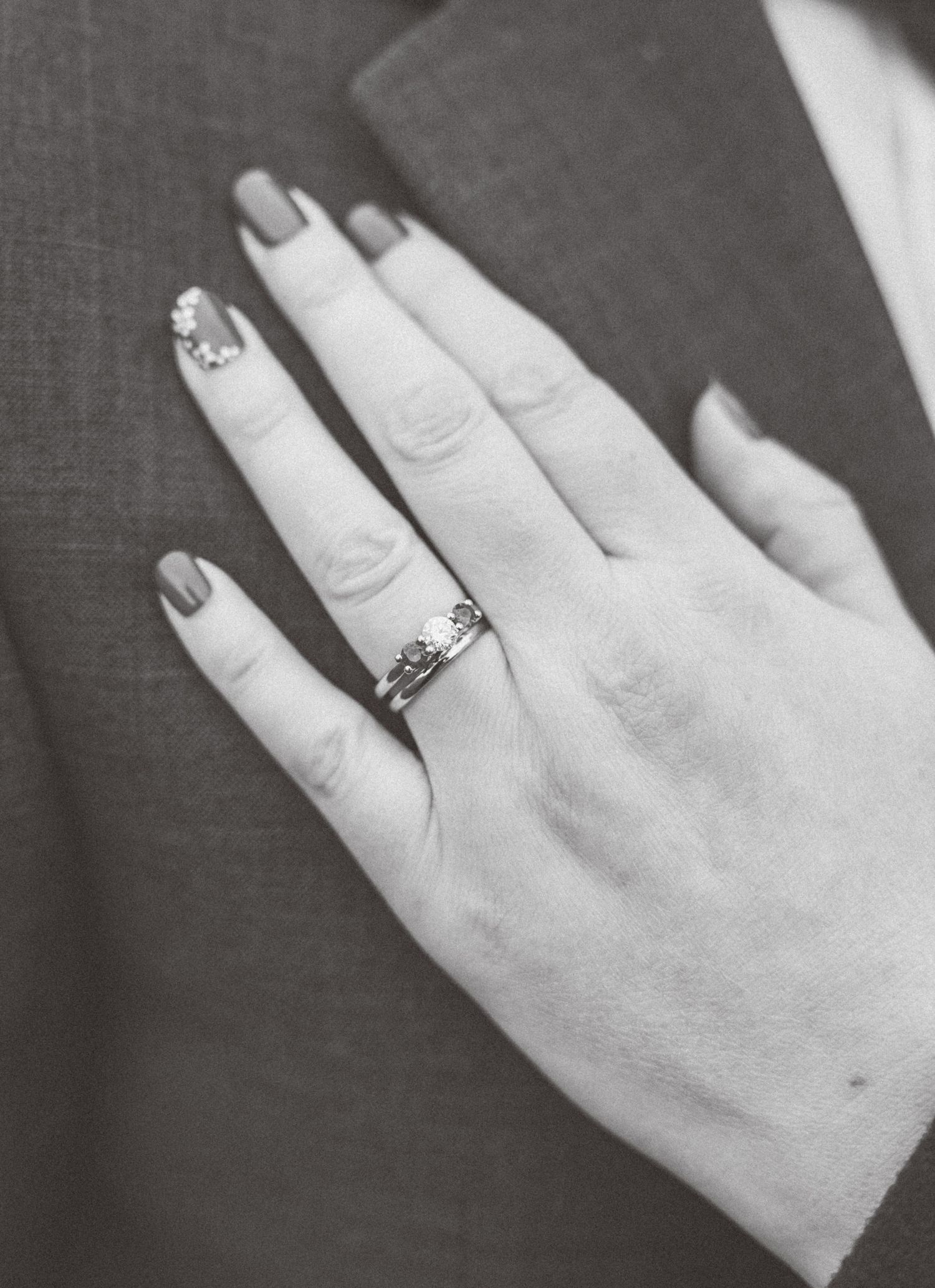 Black and white close-up of bride's hand showing elegant engagement ring and nail art.