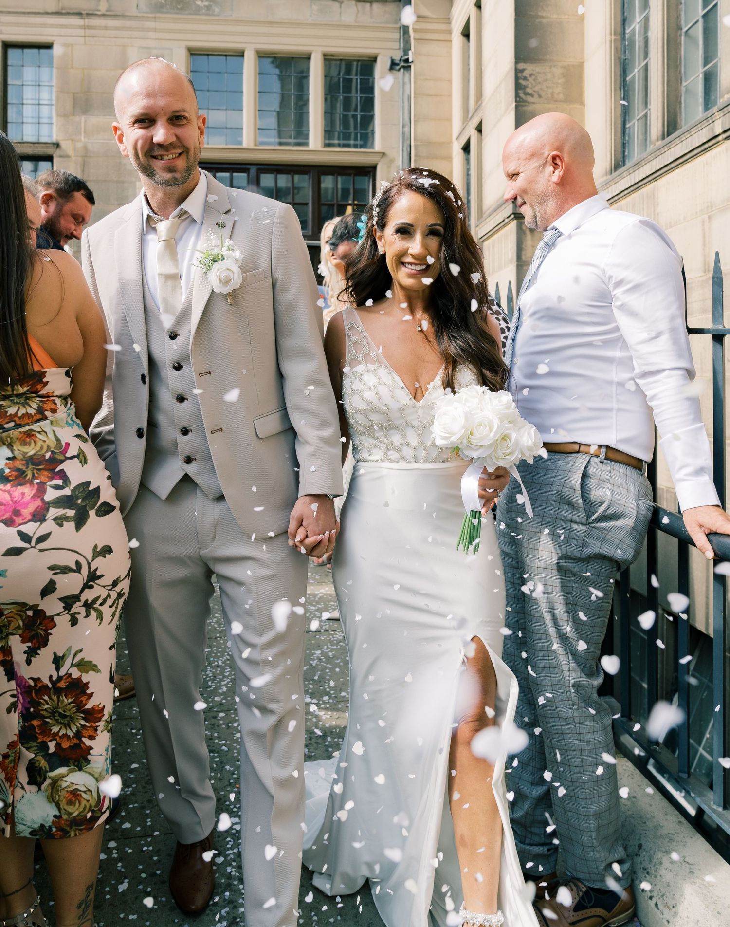 A happy wedding couple walks outside while confetti falls around them in a joyful celebration.