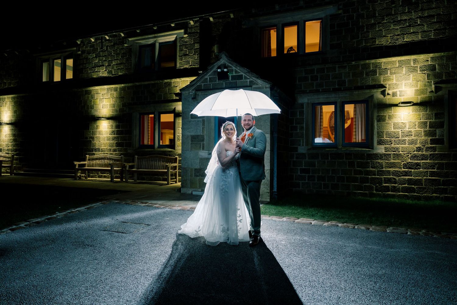 Dramatic nighttime wedding portrait under a lit umbrella against stone architecture.