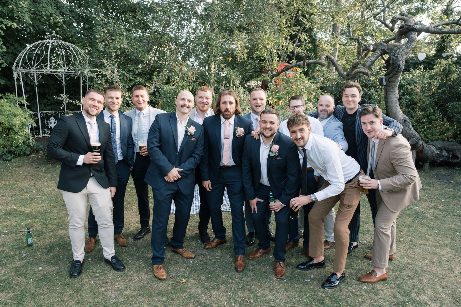 Wedding party posing for casual group photo on grassy lawn.