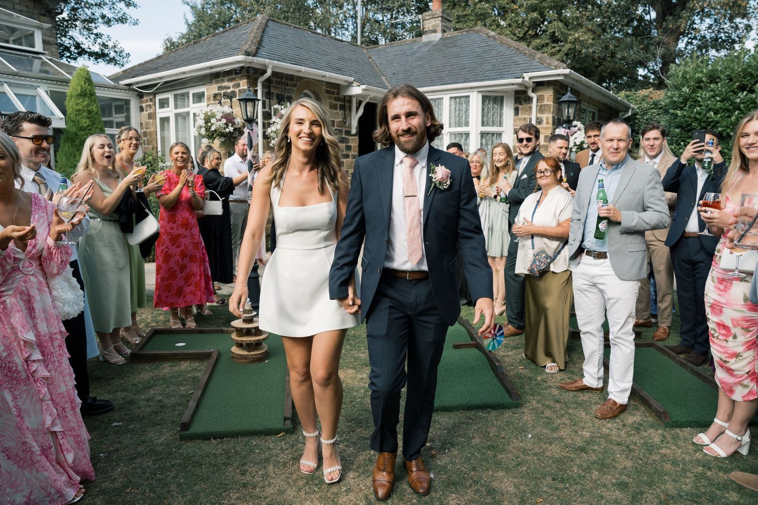 Wedding guests form a joyful receiving line on a lawn to celebrate the newlyweds' entrance at an outdoor reception.