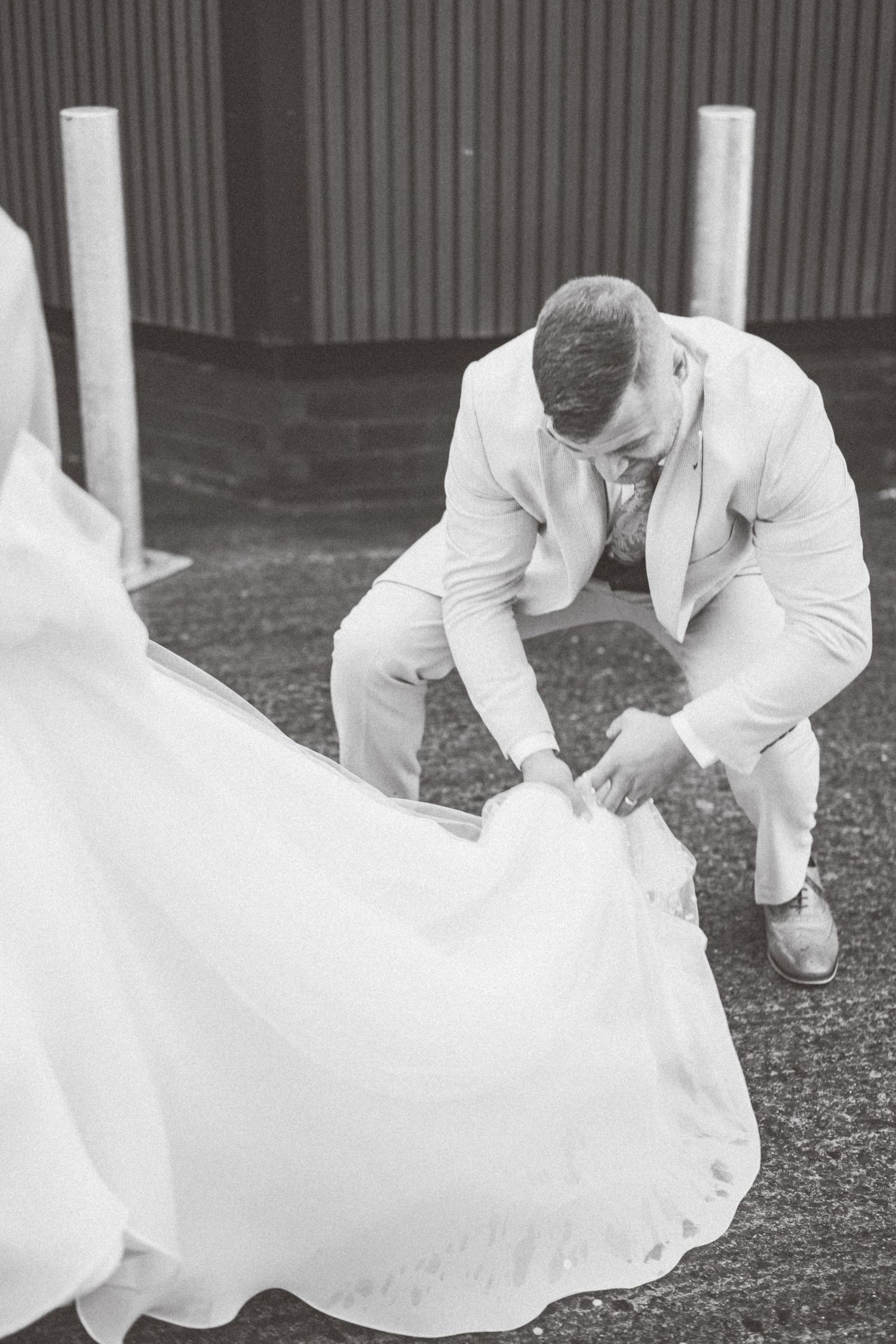 A flowing white wedding dress billows in the wind across a dark ground surface.