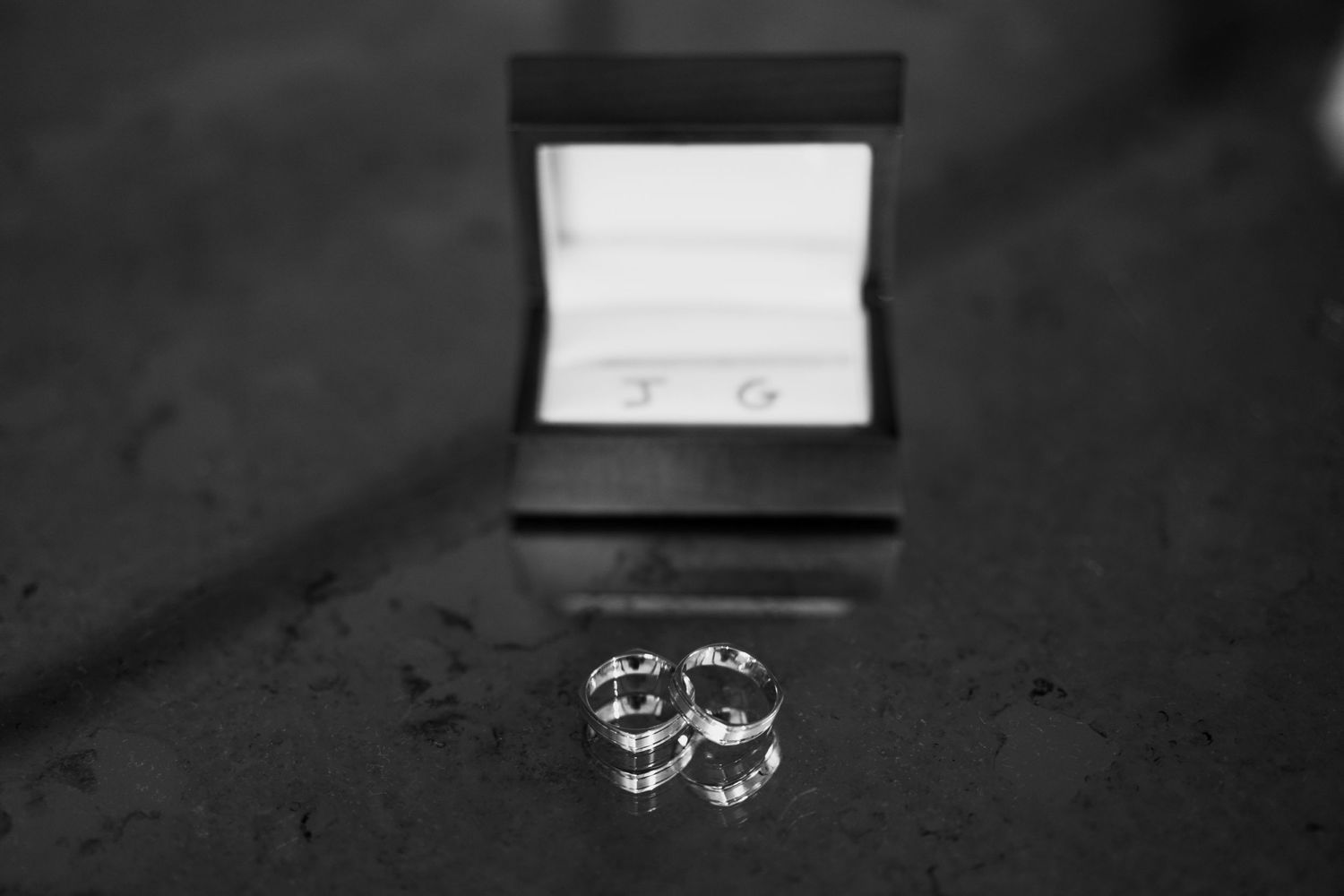 Wedding rings casting shadow next to open jewelry box in dramatic black and white photography.