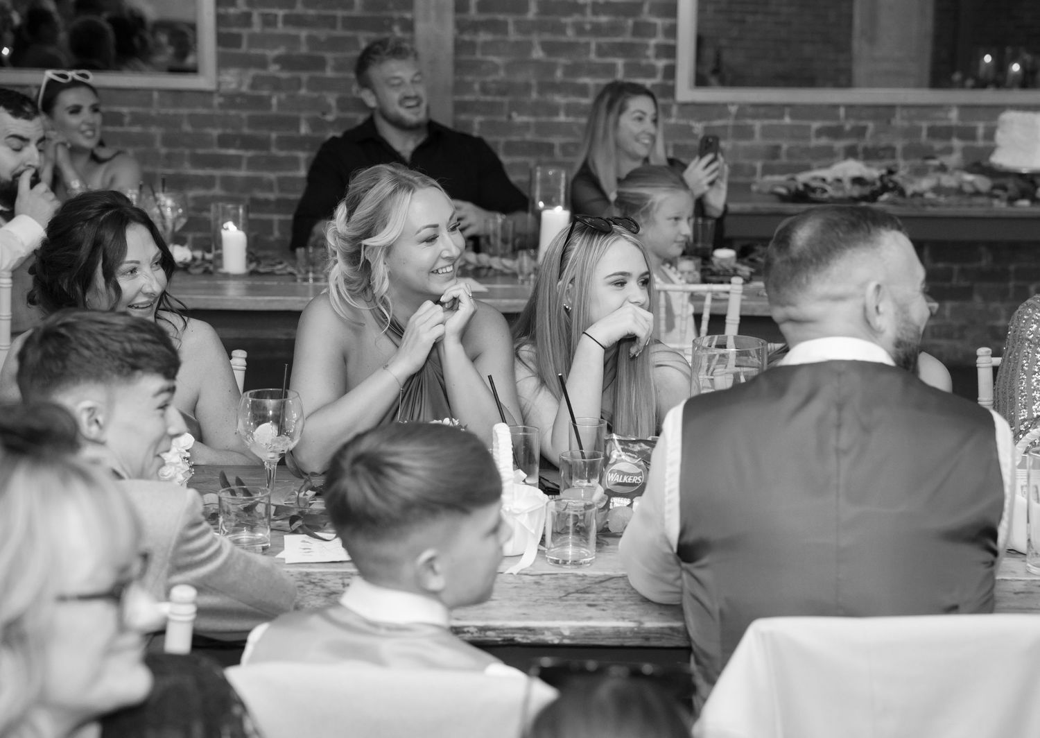 Wedding reception guests seated at tables in a rustic brick-walled venue.