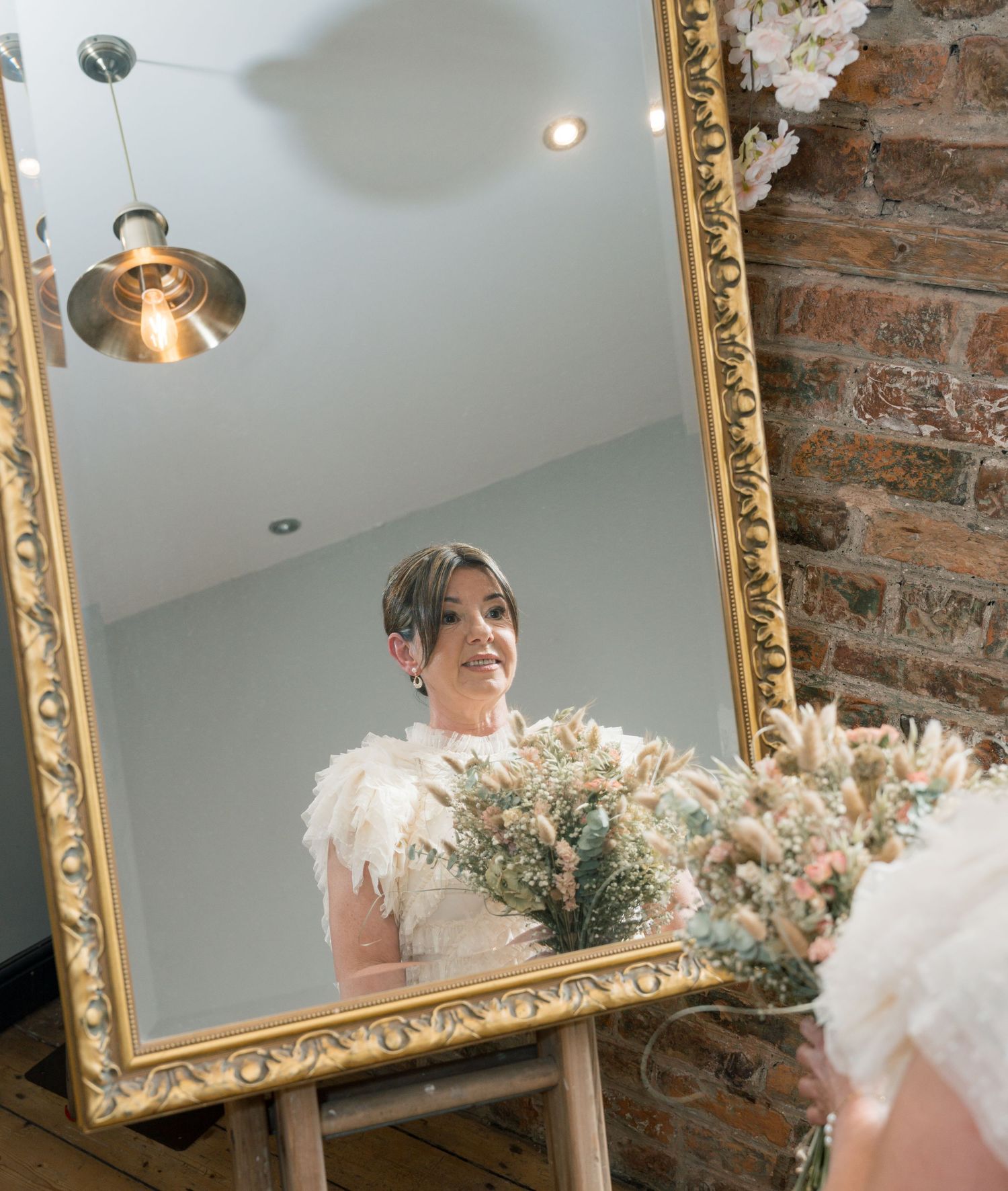 Ornate gold mirror reflects wedding decor against exposed brick wall.
