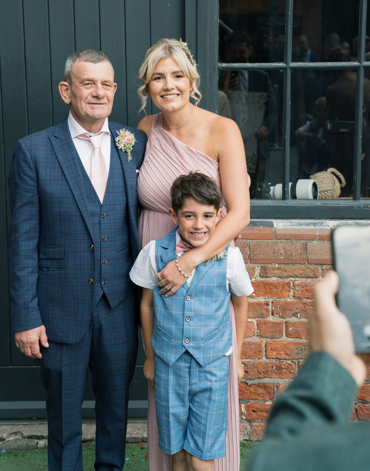Wedding party members pose against blue doors and brick wall exterior.