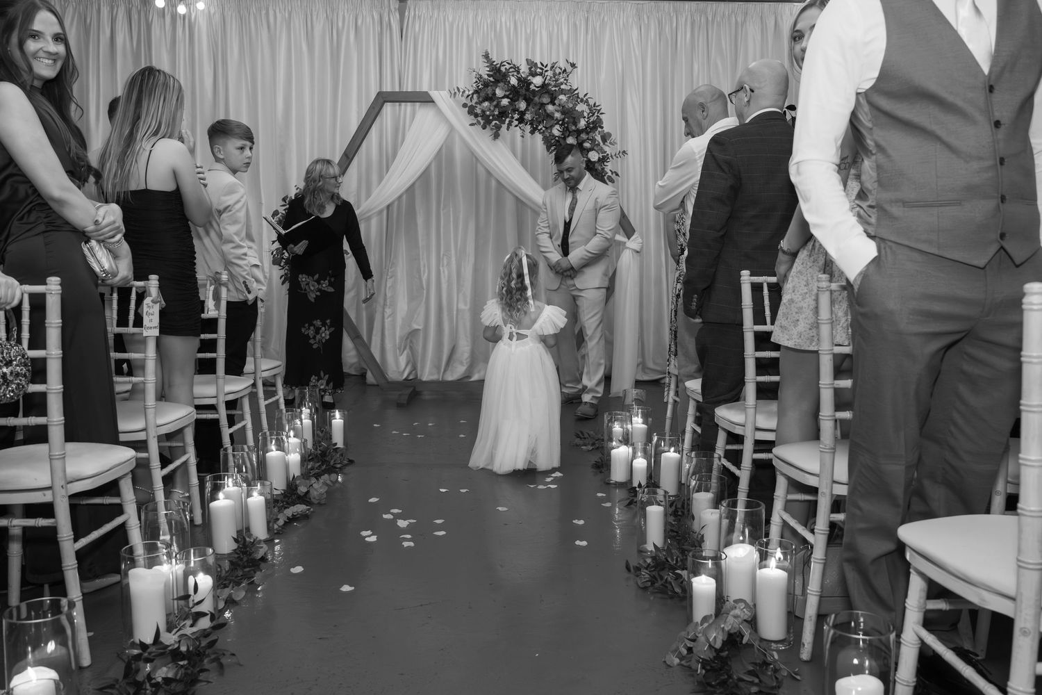A black and white wedding reception scene with guests dancing and celebrating in a venue decorated with string lights.