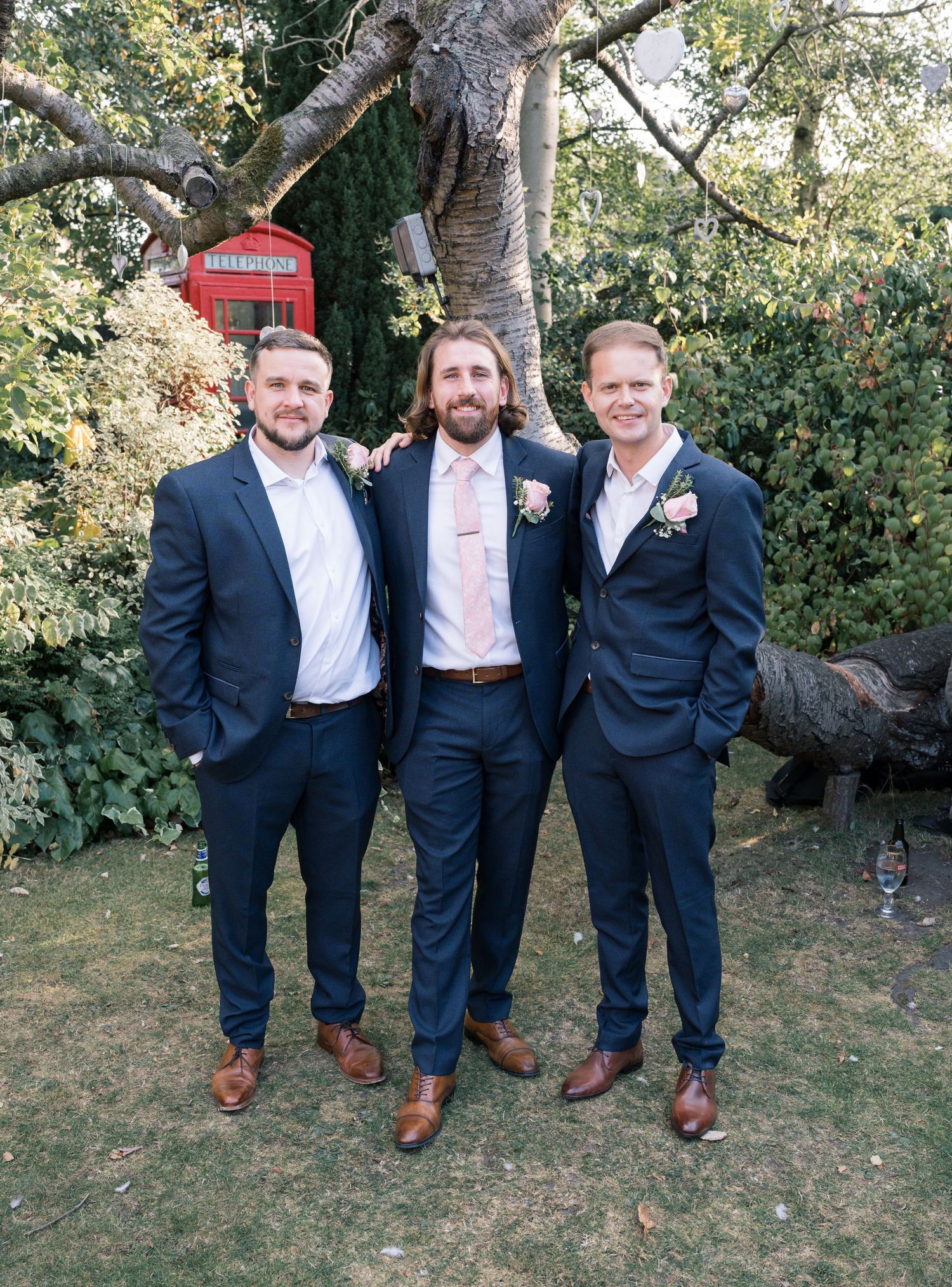 Groomsmen in navy suits and brown shoes pose casually on grass.