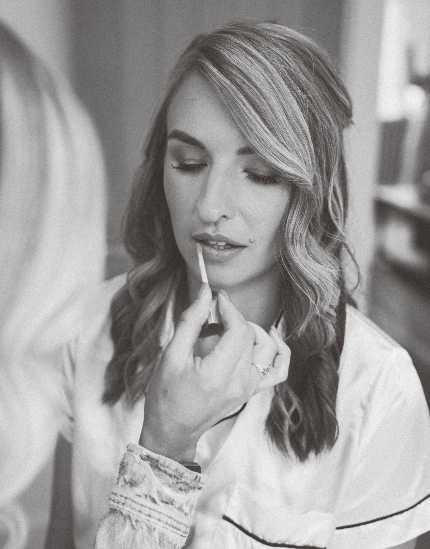 Black and white photo showing makeup being applied with a brush in a soft, natural lighting setting.