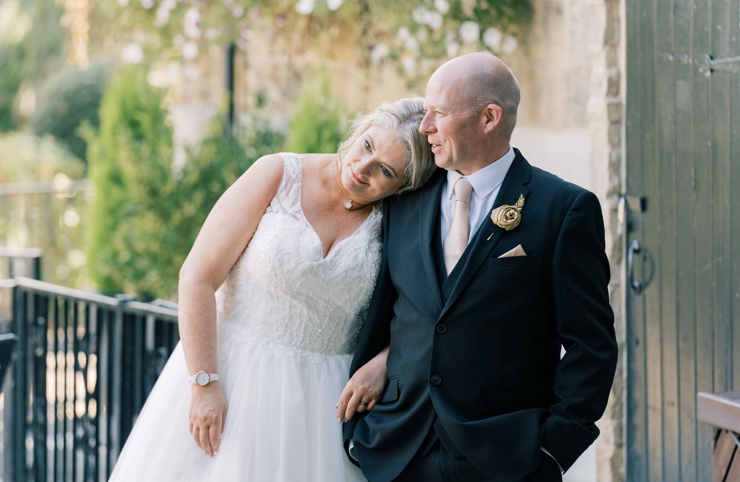A tender moment between newlyweds leaning against a rustic stone wall outdoors.