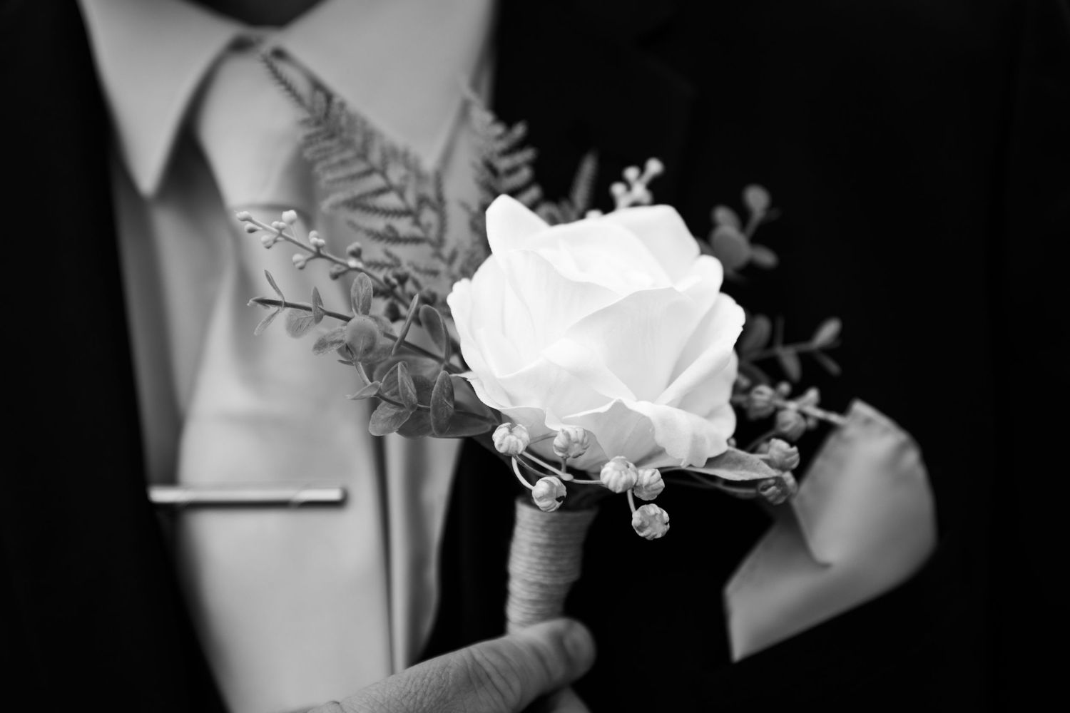 Close-up of a white rose boutonniere with delicate silver ferns against formal attire.
