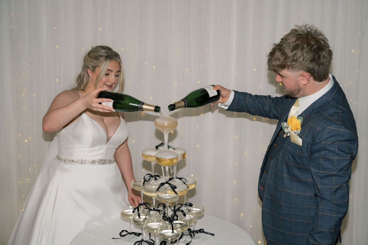 Bride and groom pouring champagne into a tower of glasses at their wedding reception.