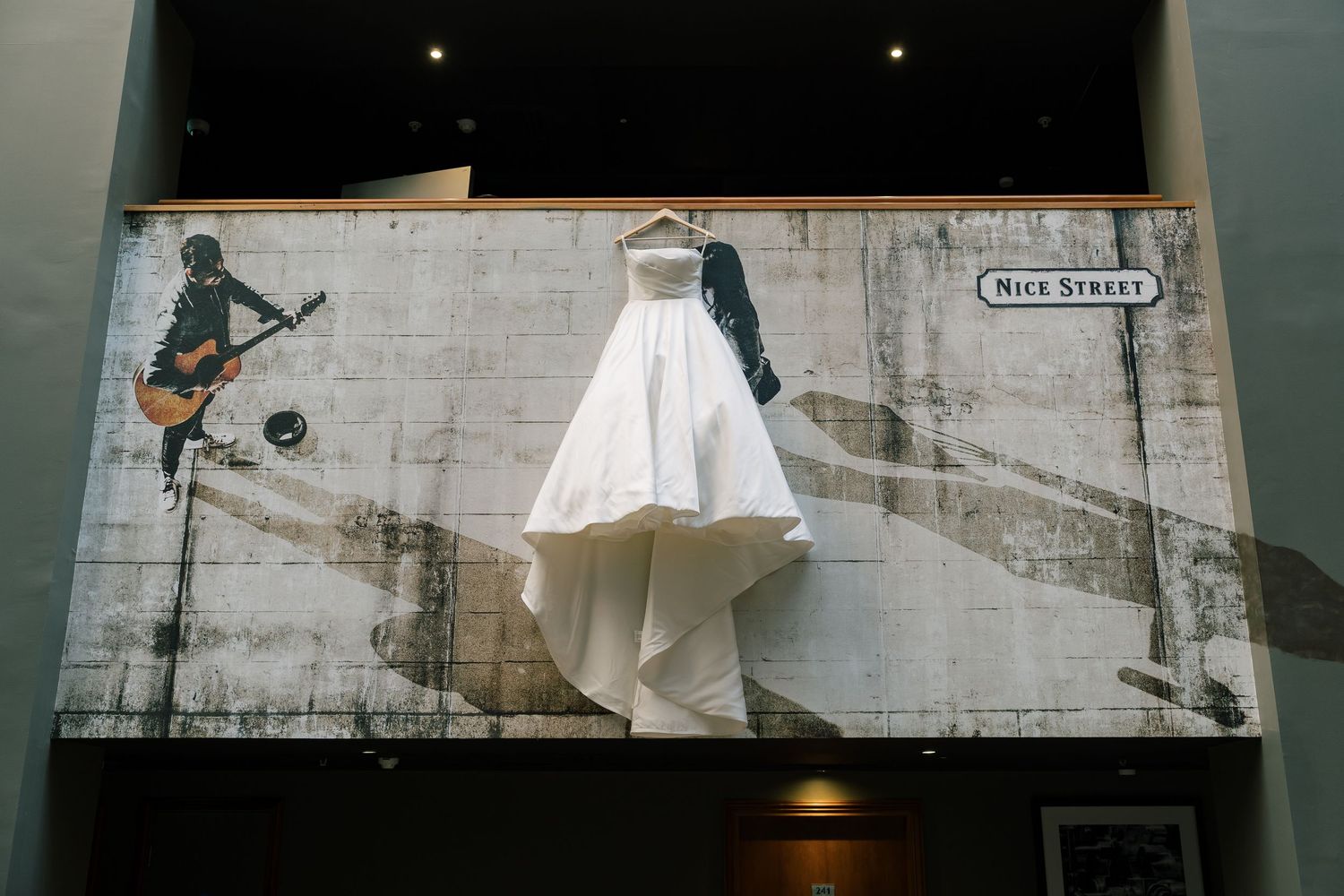 Wedding dress displayed on wall with street art mural background.