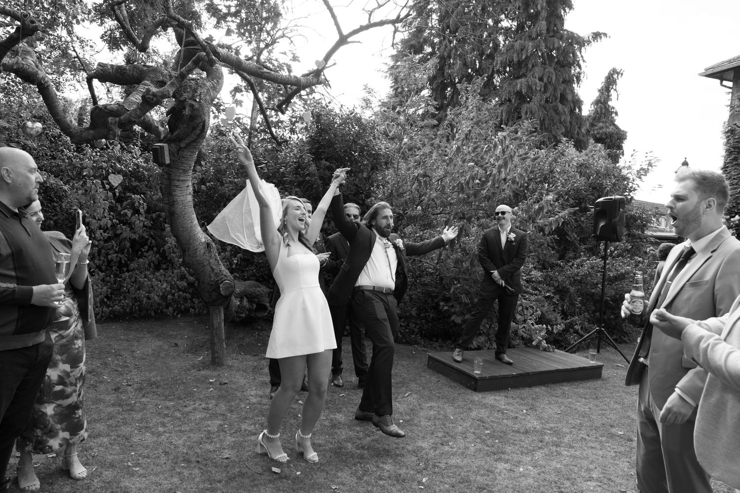 Wedding guests gather outdoors in a garden setting during a celebration.