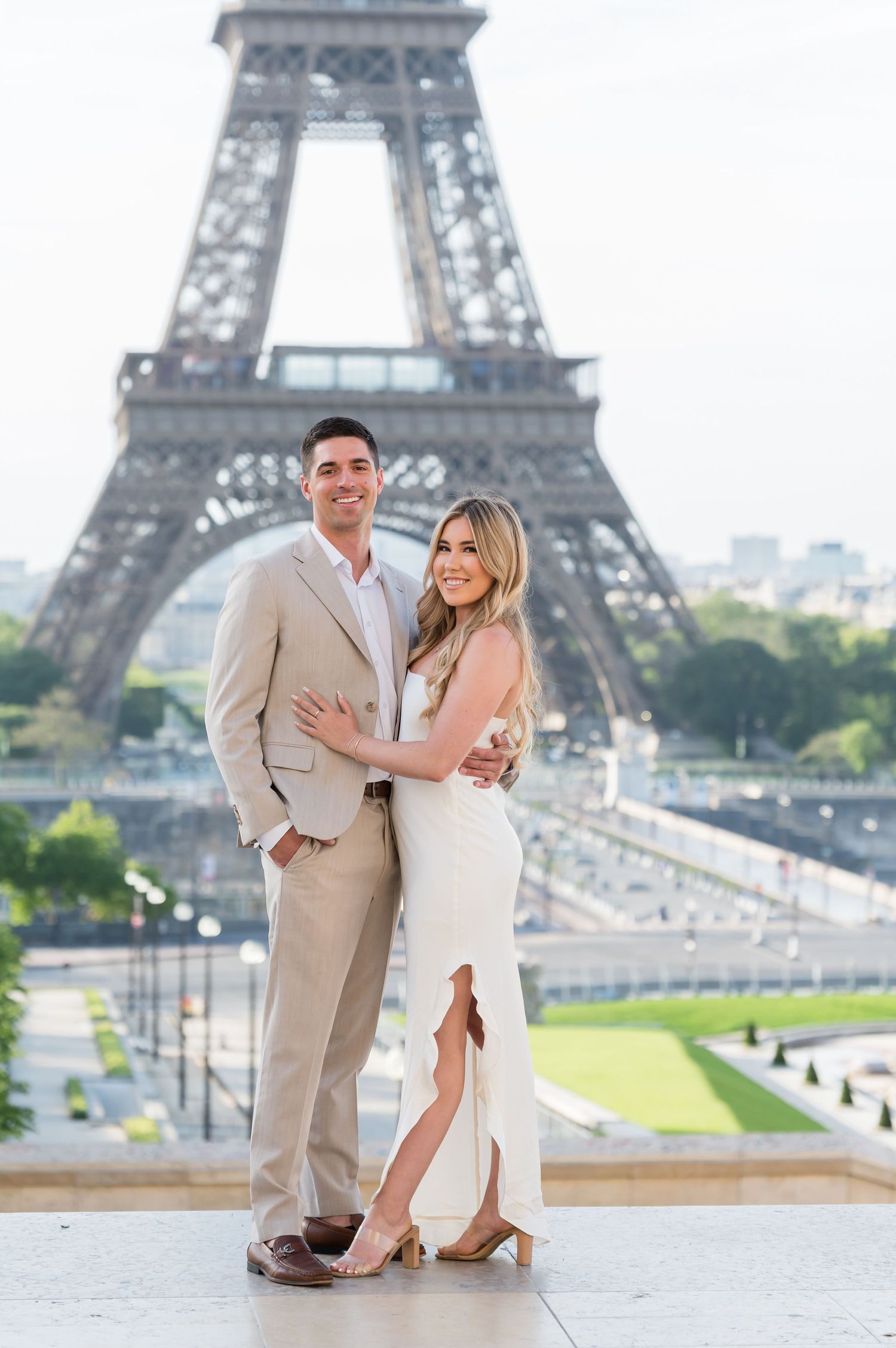 A romantic couple poses for a photo in front of the Eiffel Tower in Paris wearing elegant formal attire.